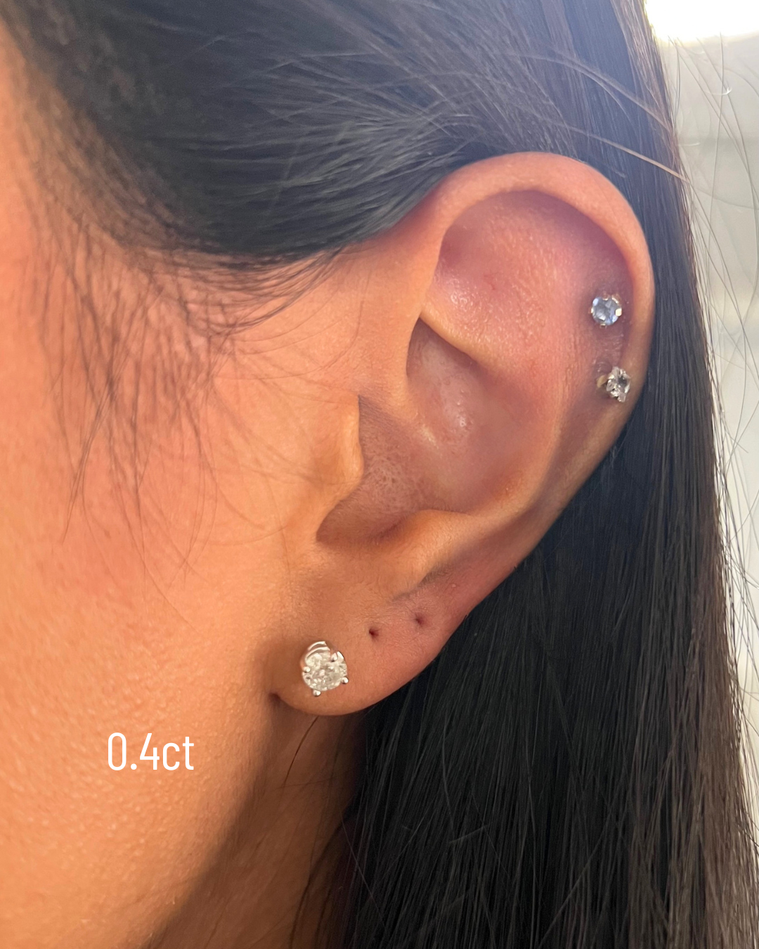 Close-up of an ear wearing a diamond stud earring with '0.4ct' label.