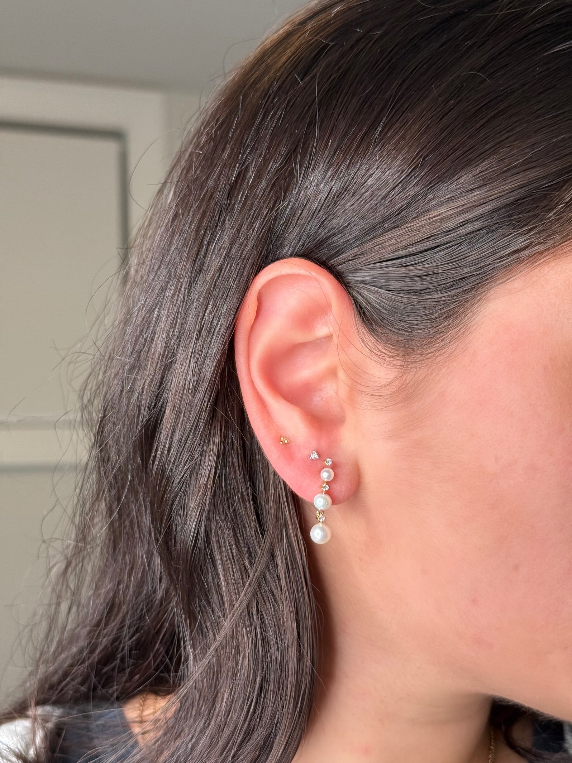 Close-up of an ear stack featuring pearl and diamonds, and two simple gold and diamond studs. 