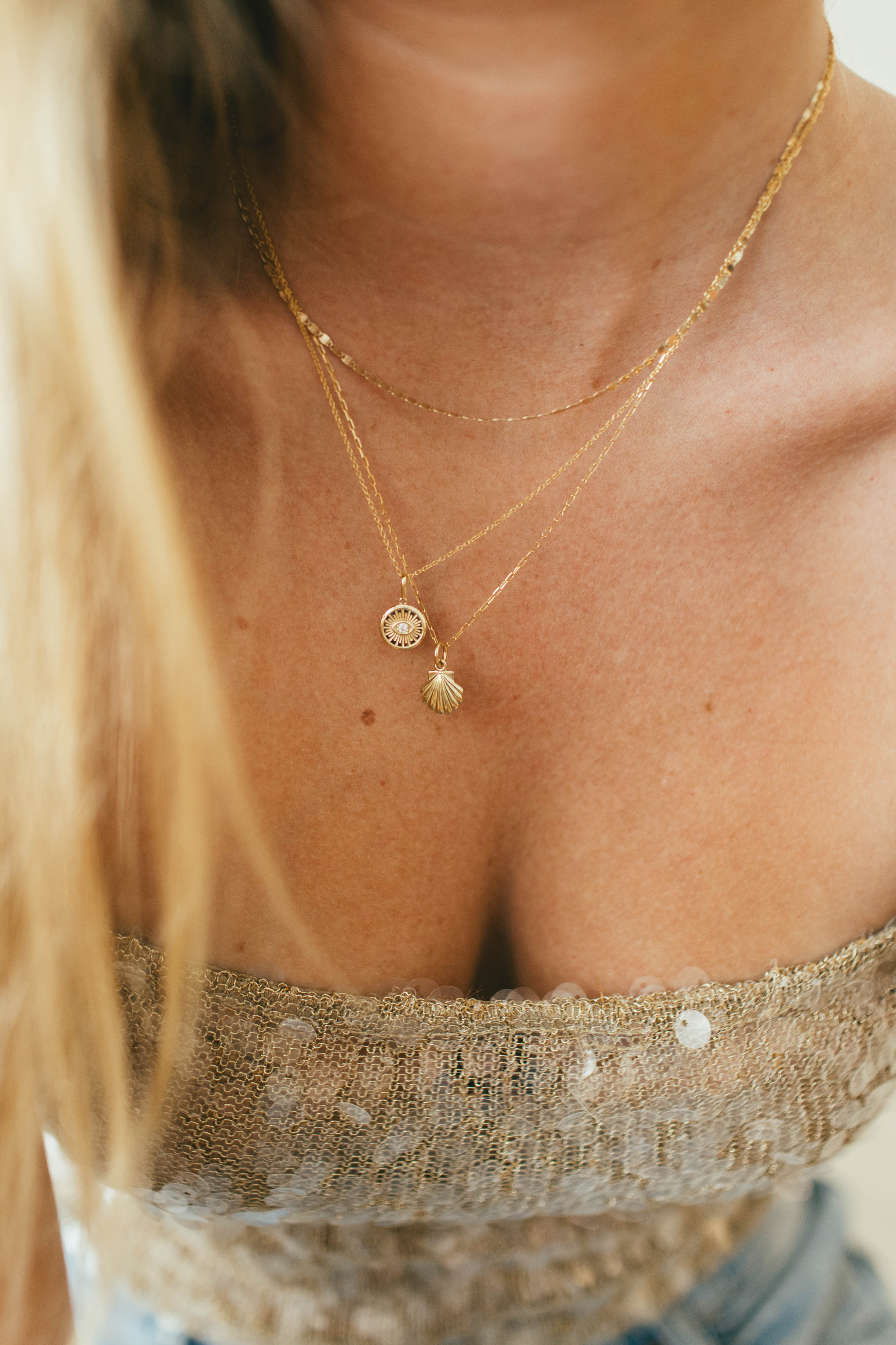 Close-up of a person wearing a gold necklace with a small evil eye and shell pendant.