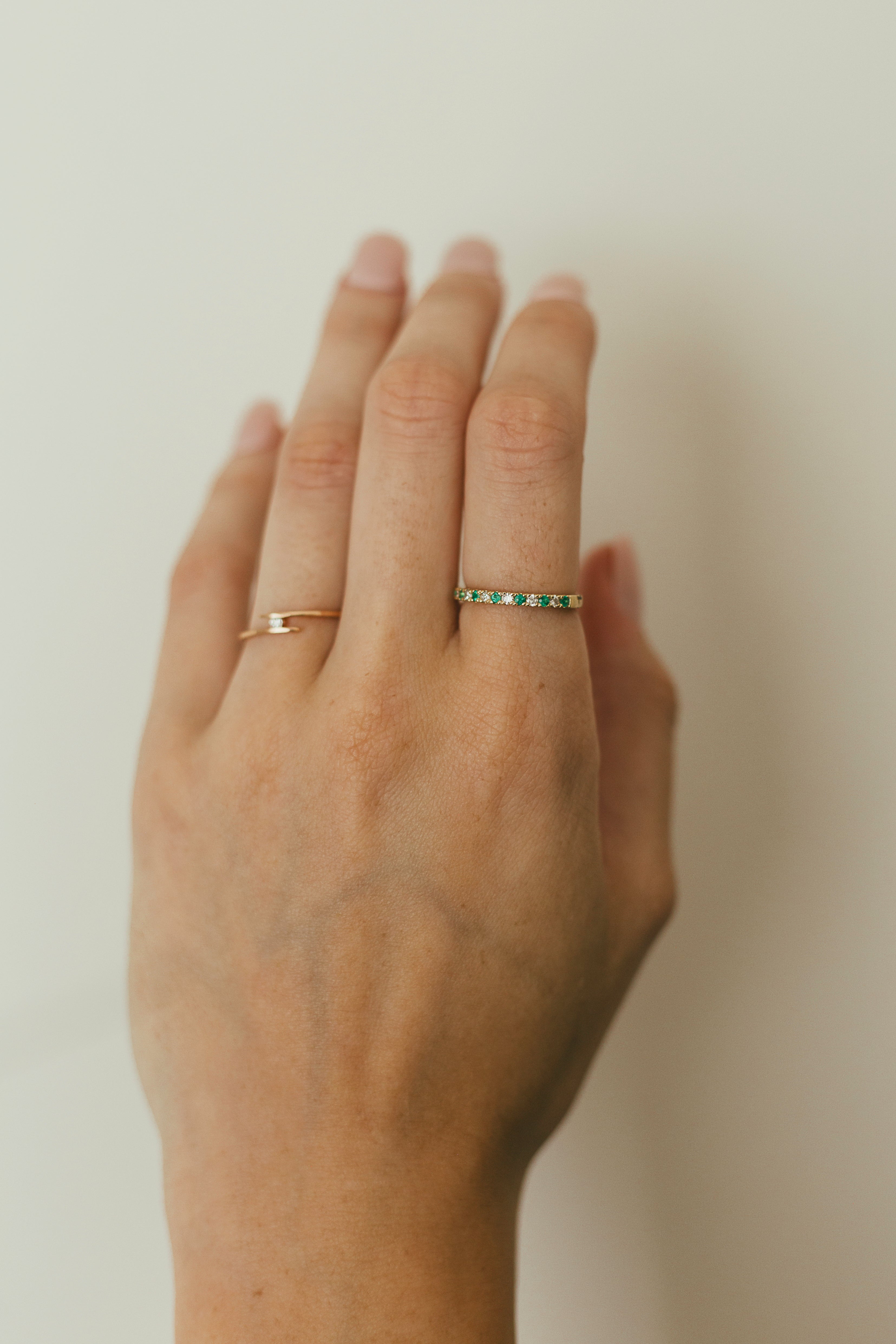 A person's hand wearing an alternating diamond and birthstone ring against a neutral background.