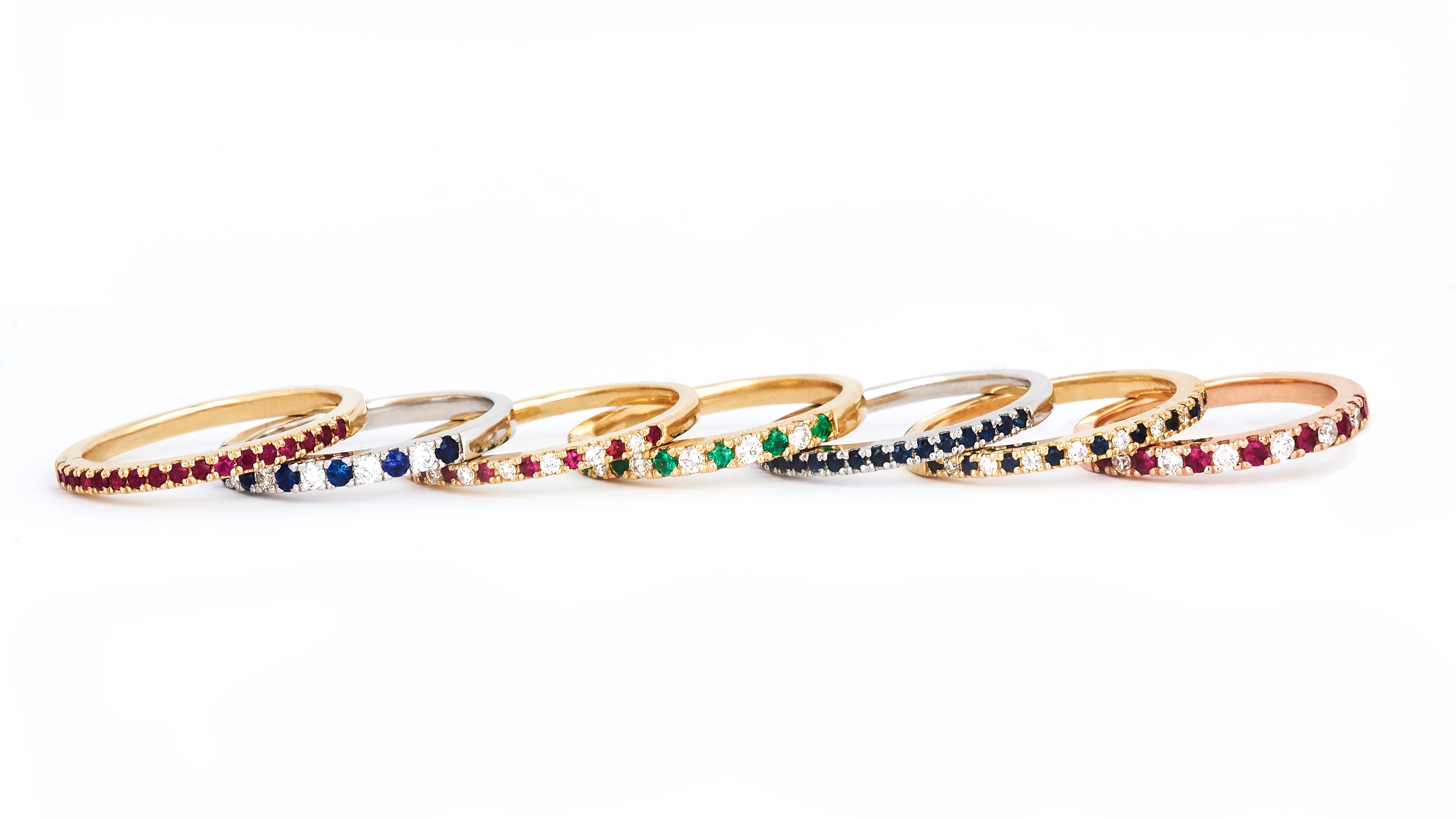 A row of seven alternating diamond and birthstone rings against a white background.