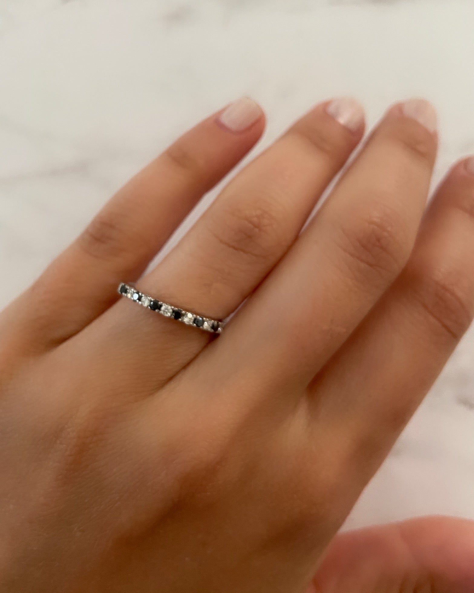A person's hand wearing an alternating diamond and birthstone ring against a neutral background.