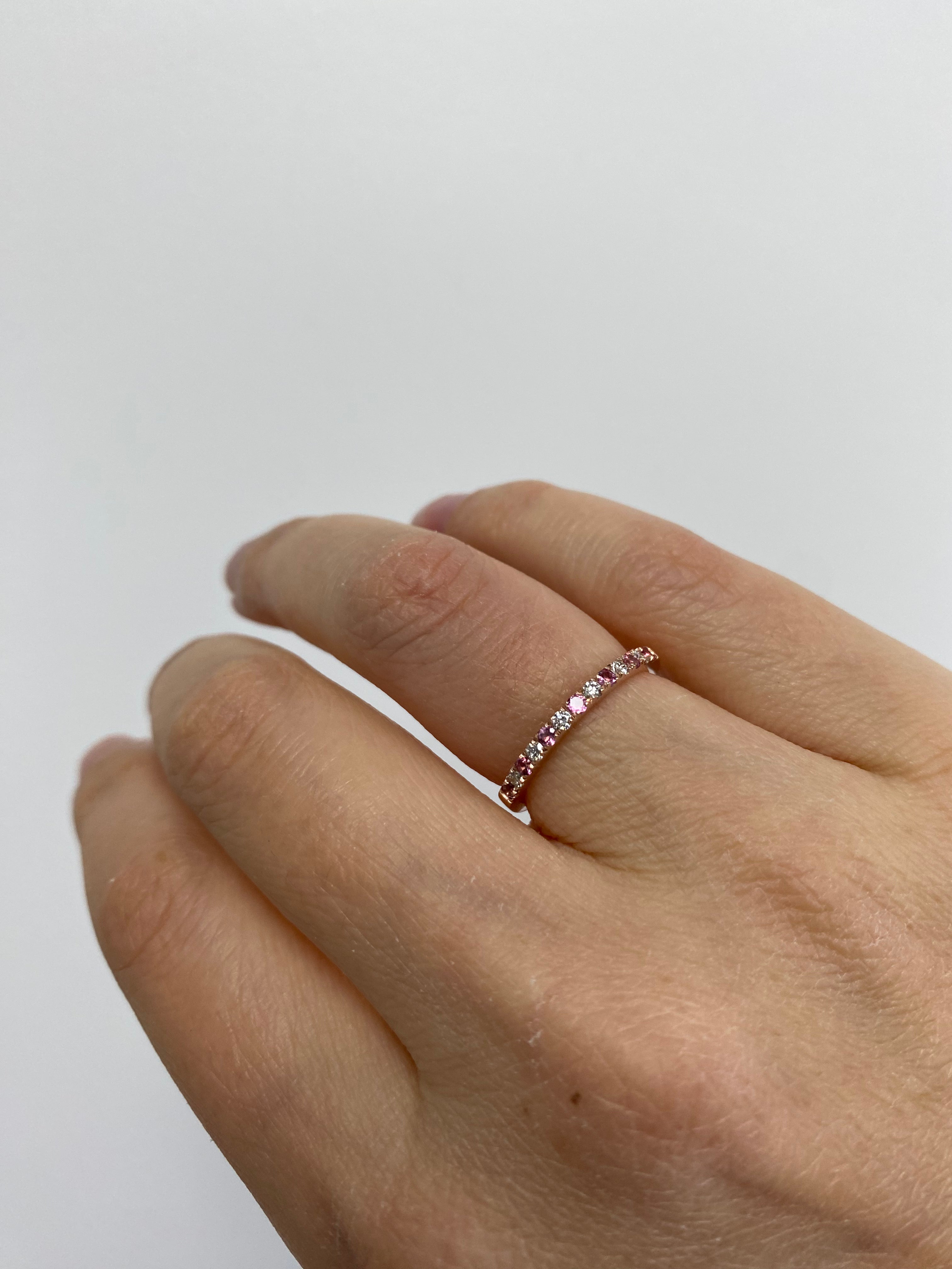 A person's hand wearing an alternating diamond and birthstone ring against a neutral background.