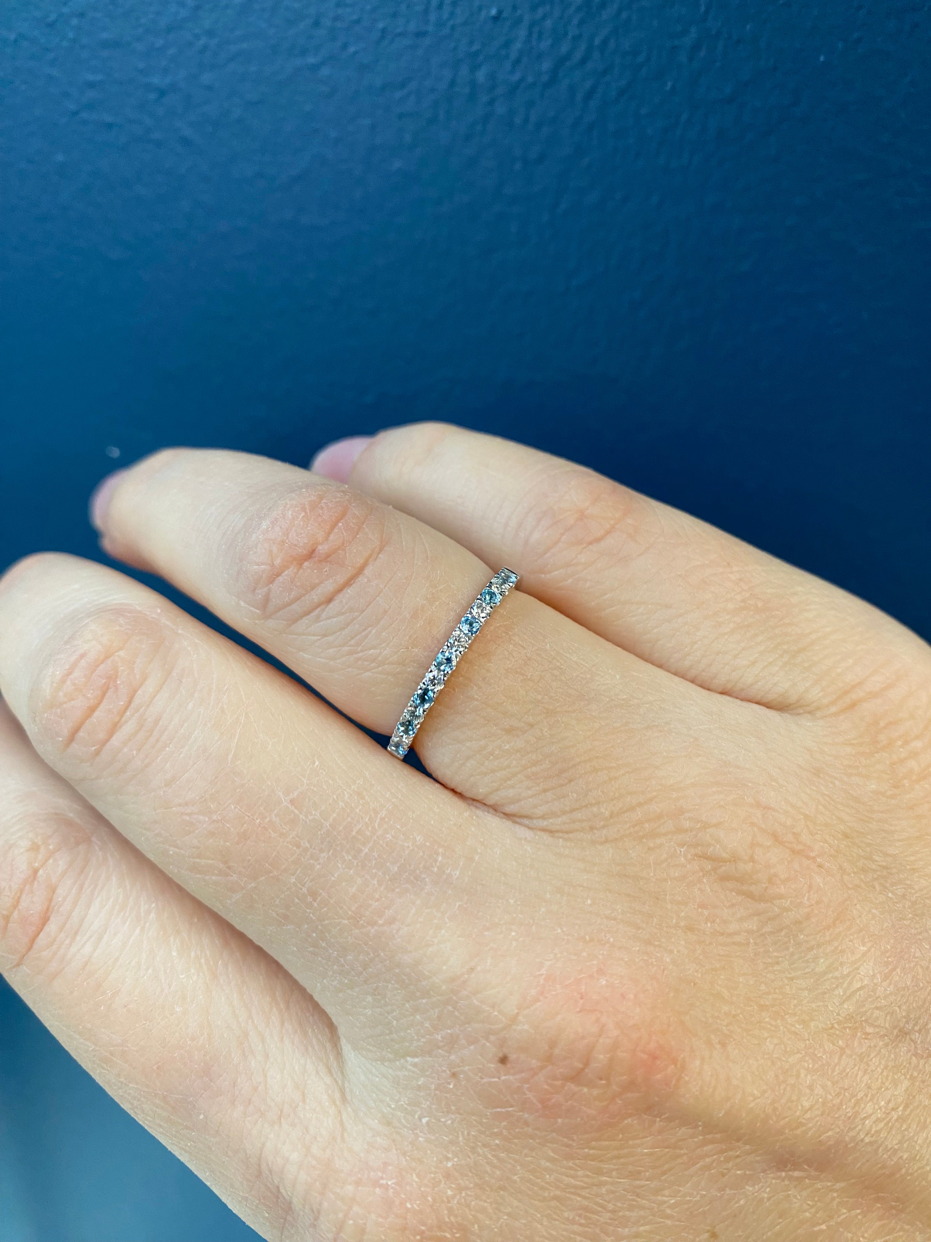A person's hand wearing an alternating diamond and birthstone ring against a neutral background.