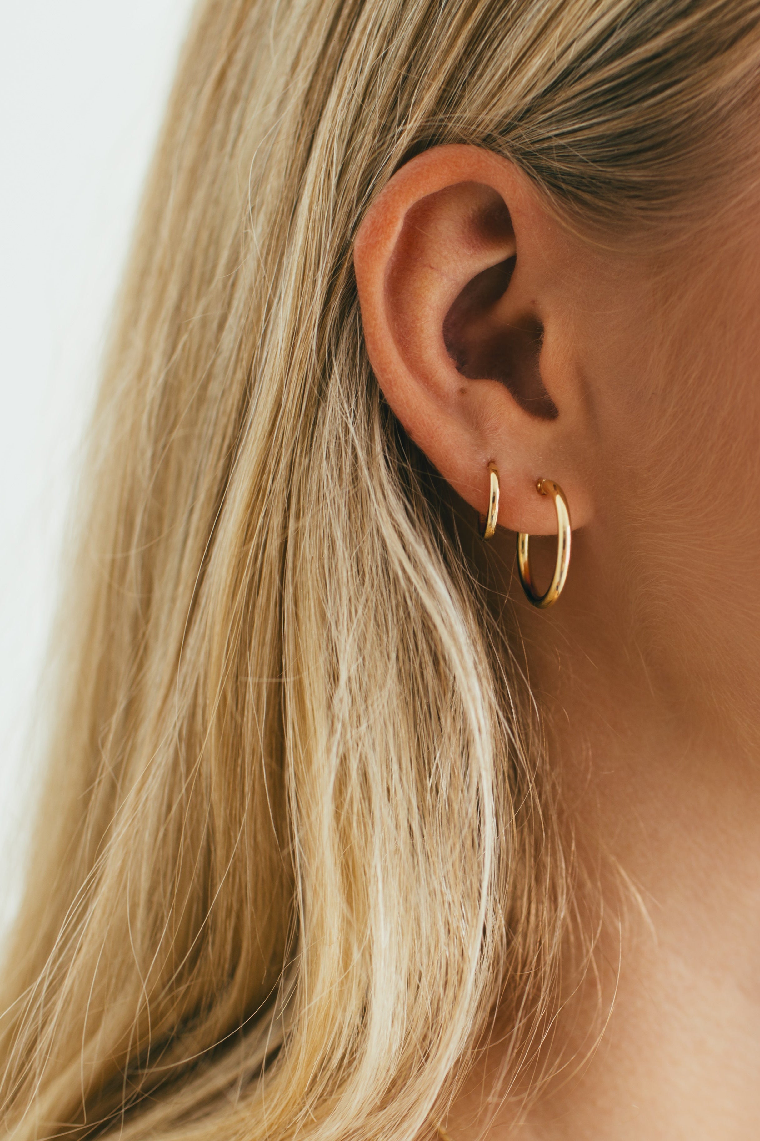 side profile of girl wearing a gold hoops earring stack 