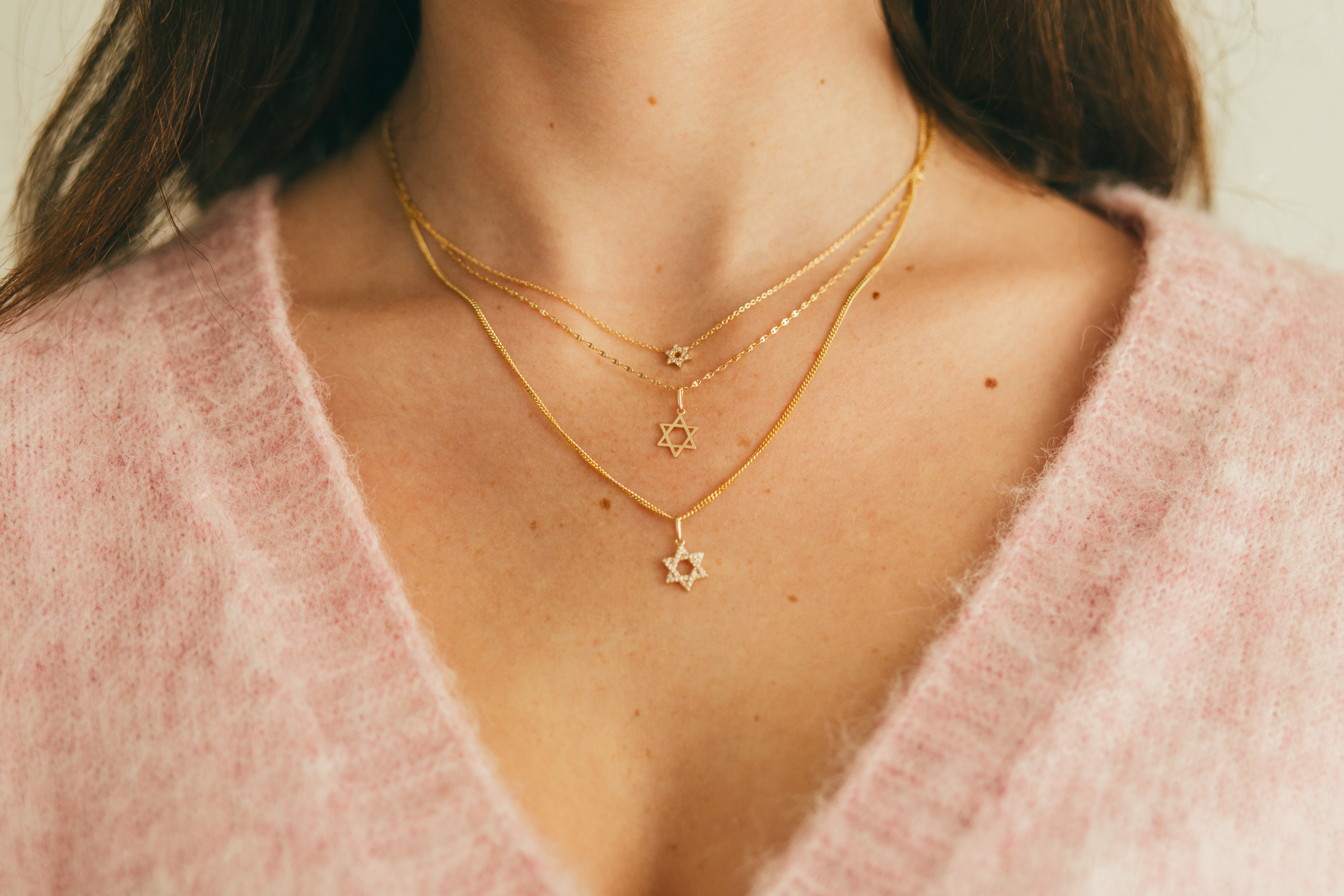 close up of person wearing a layered look of star of david necklaces and pendants