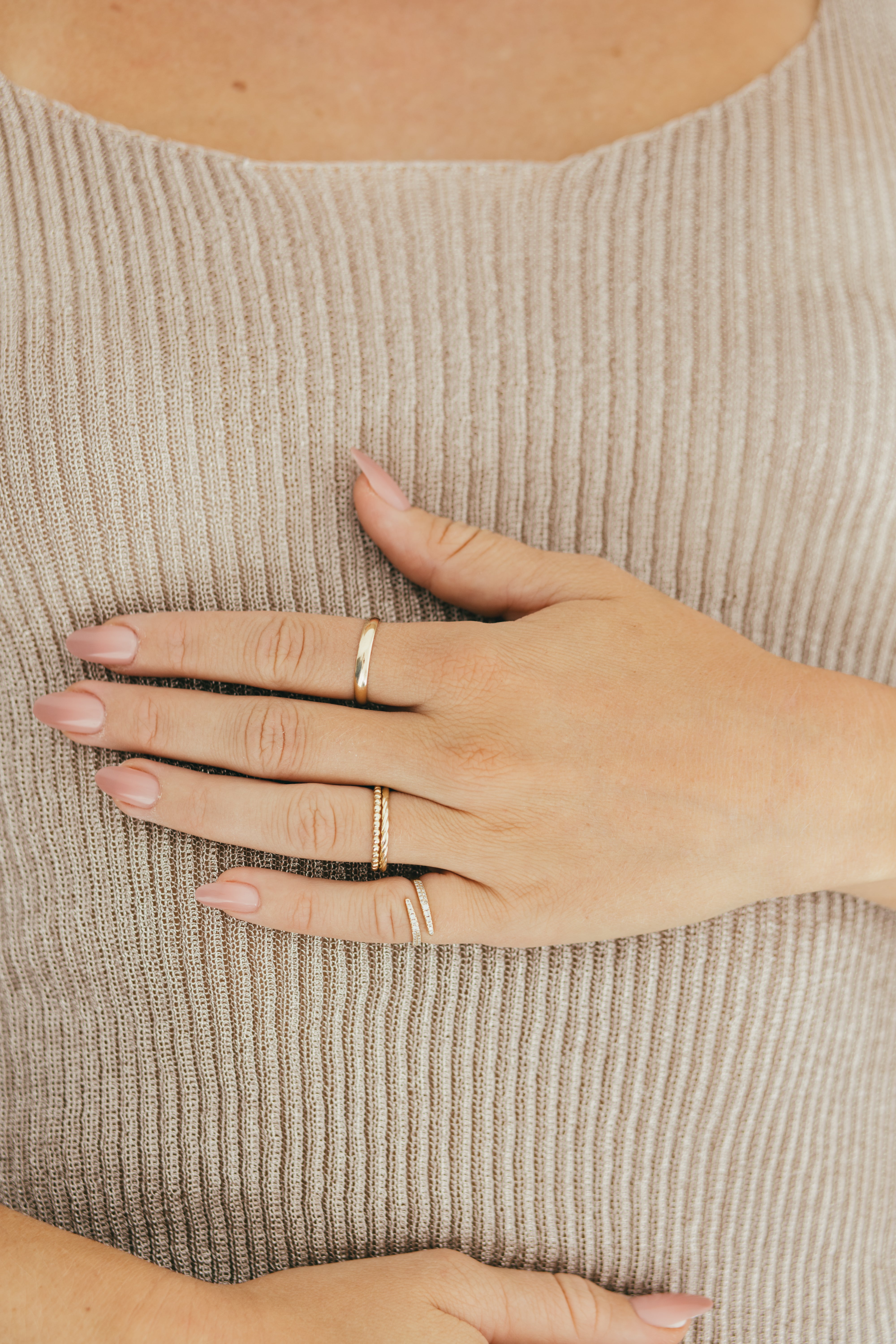Multiple gold rings styled on a person's hand against a beige top.