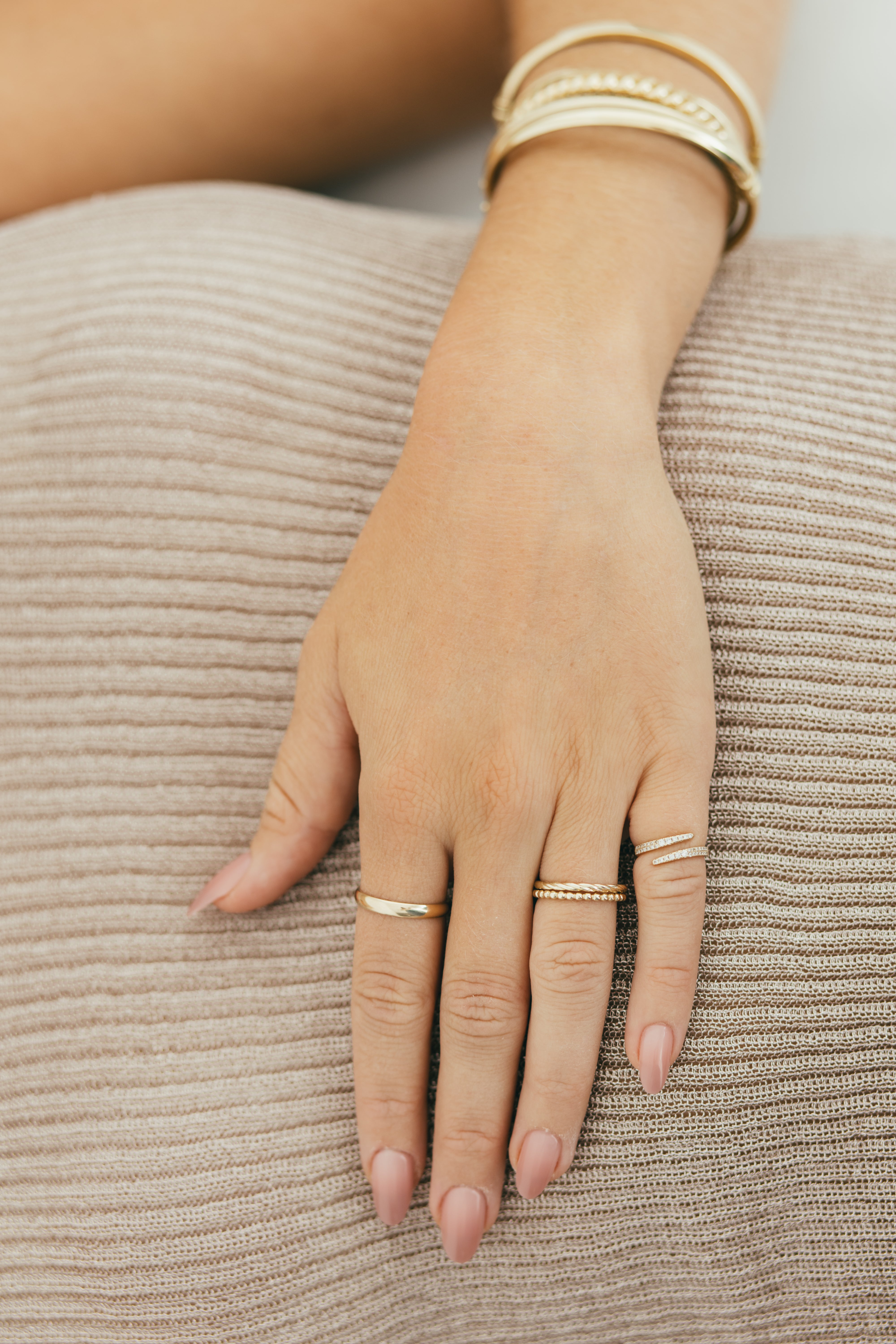 A hand wearing multiple gold rings on a textured beige top.