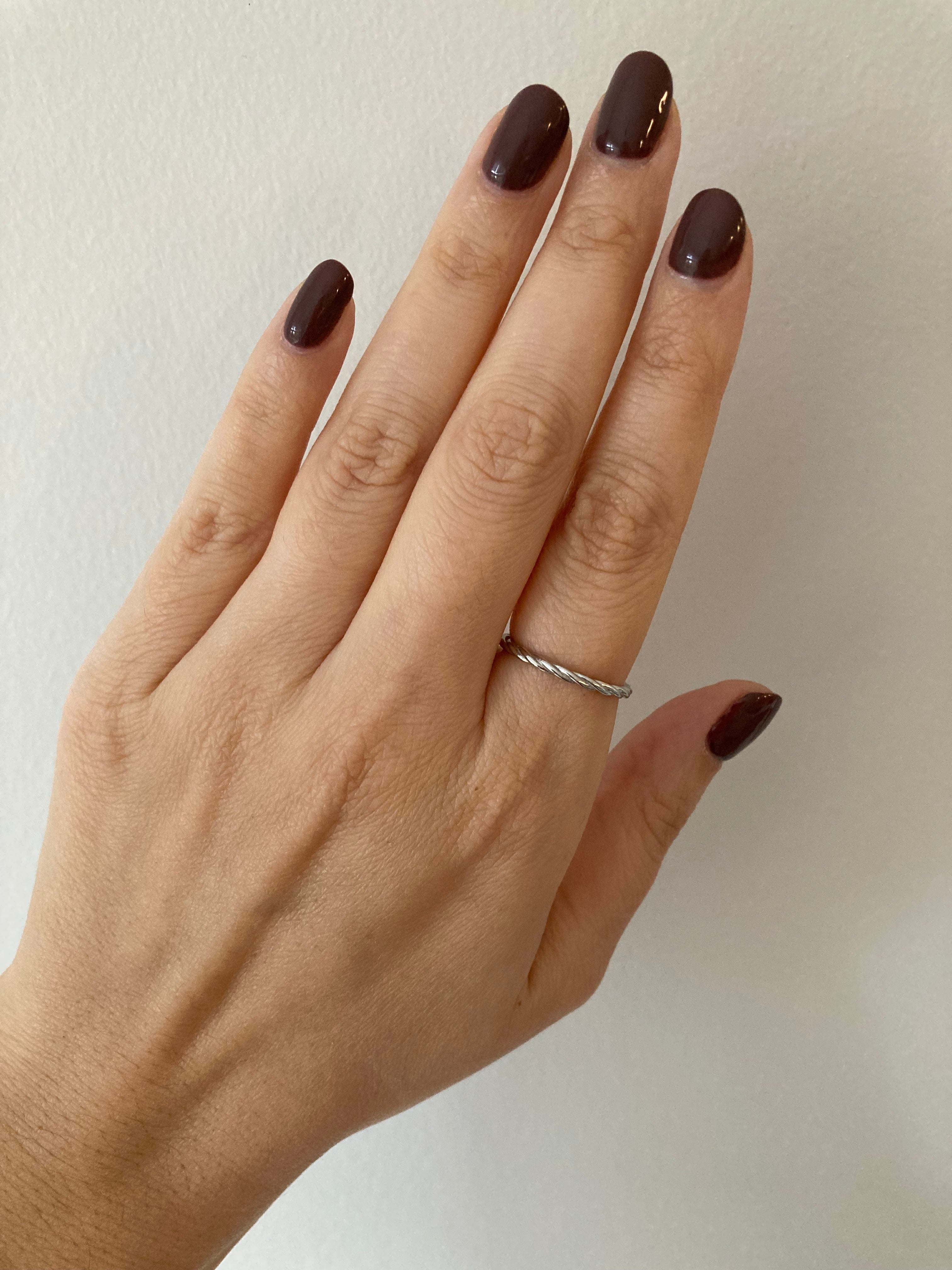A white gold twisted rope ring worn on a person's finger against a neutral background.