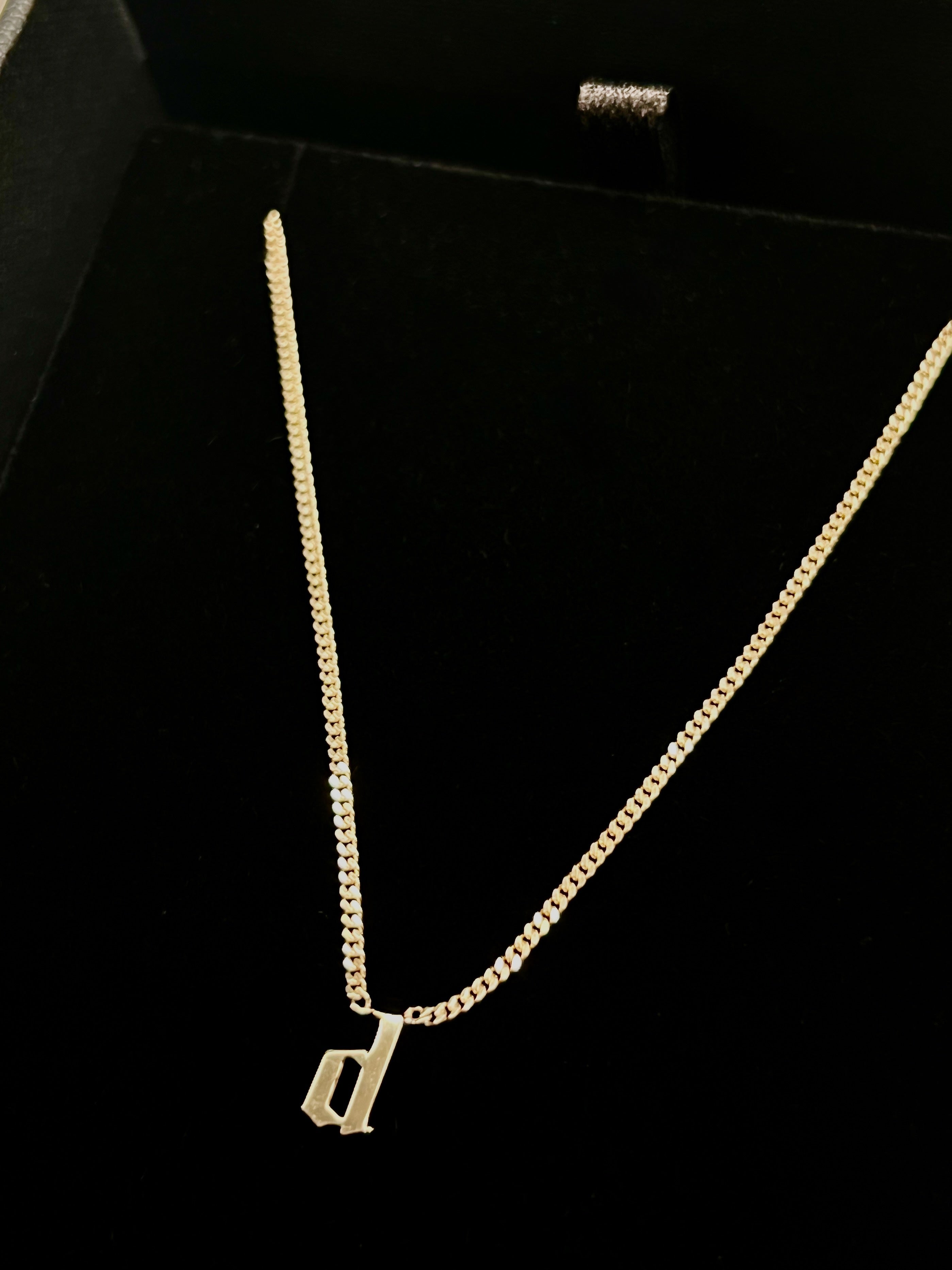 A gold chain necklace with a cutout initial 'd' pendant.