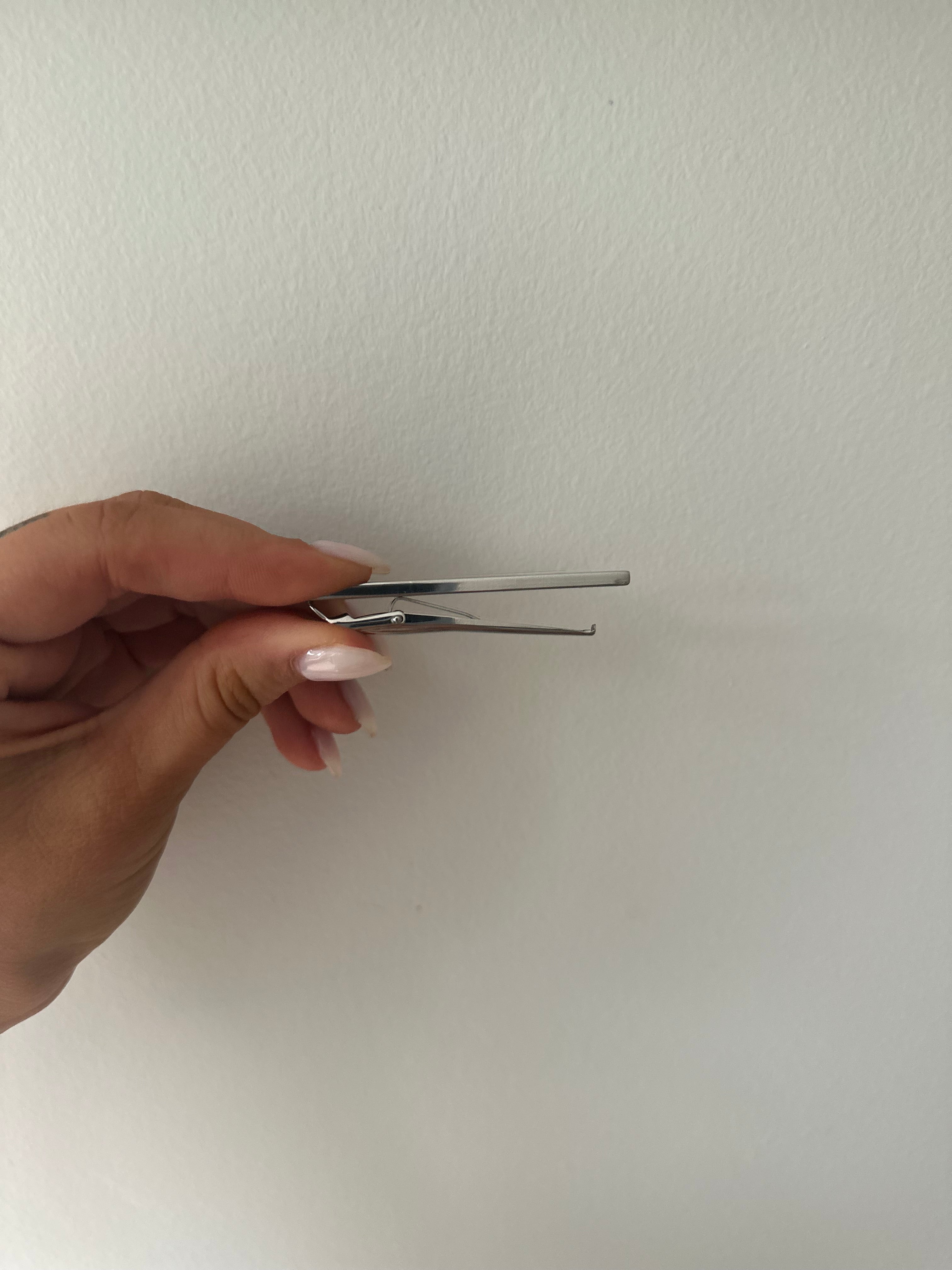 A side profile of a sterling silver bordered tie bar held between fingers against a neutral background.