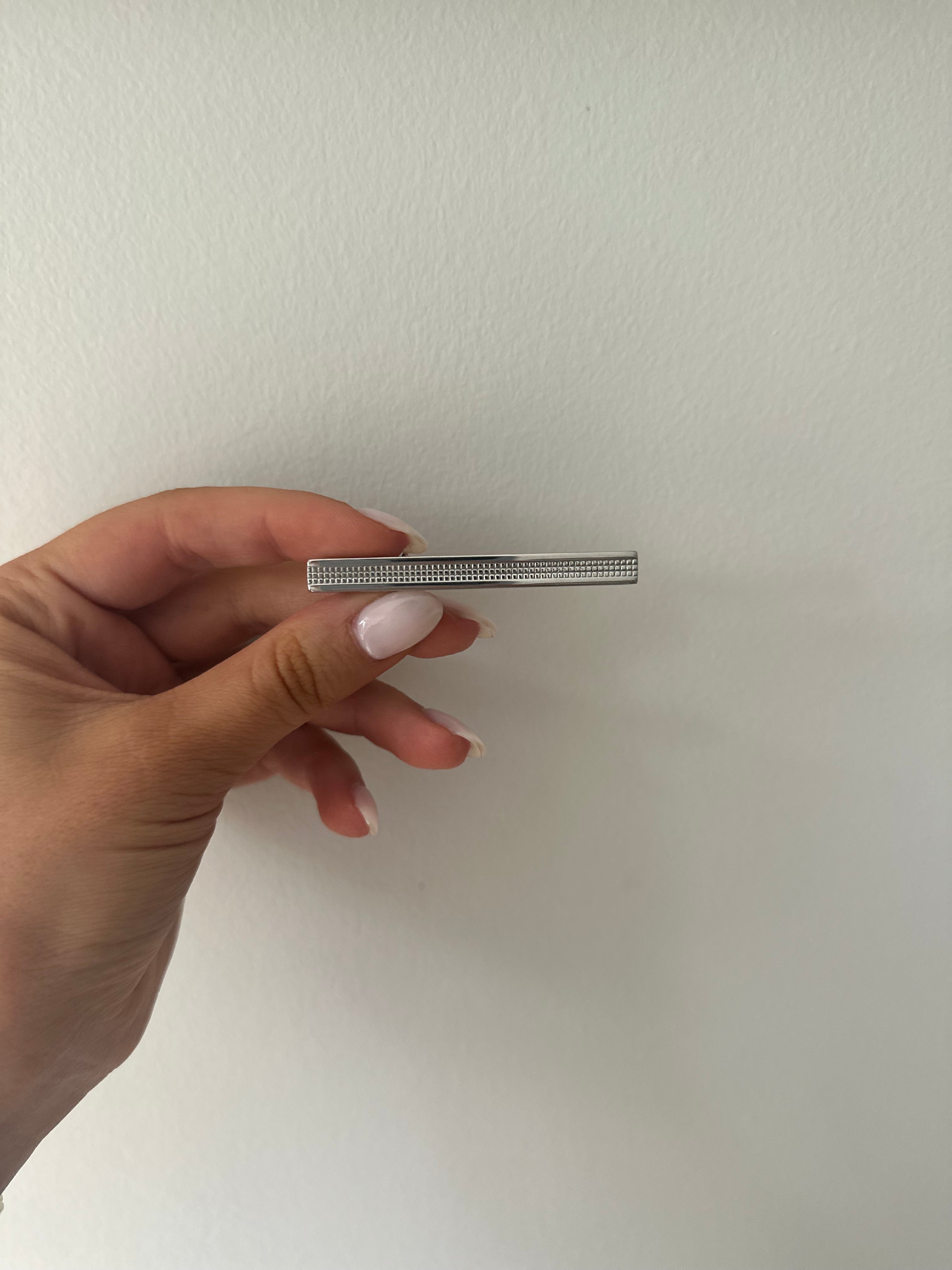 A sterling silver bordered tie bar held between fingers, with a textured design and smooth borders.