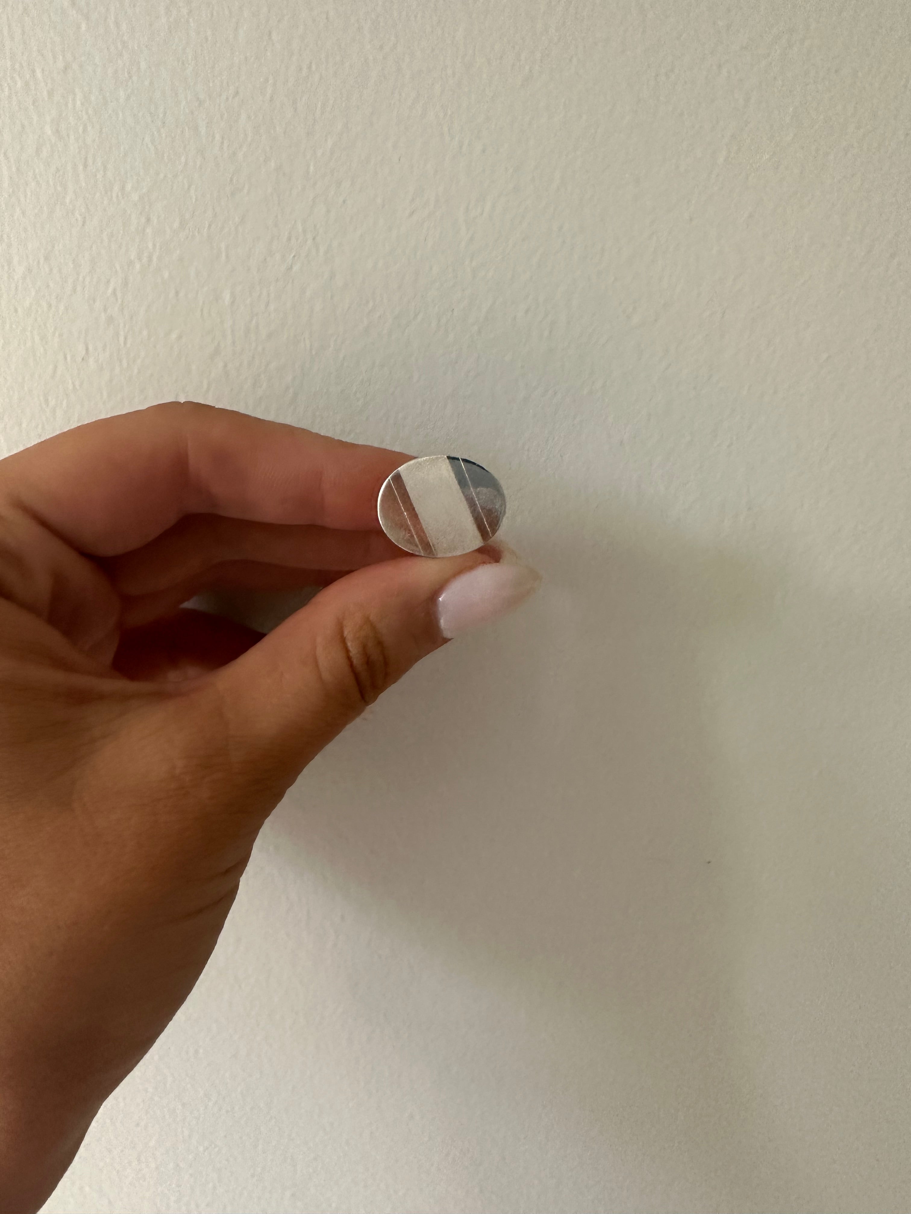 A sterling silver oval cufflink held between fingers against a neutral background.