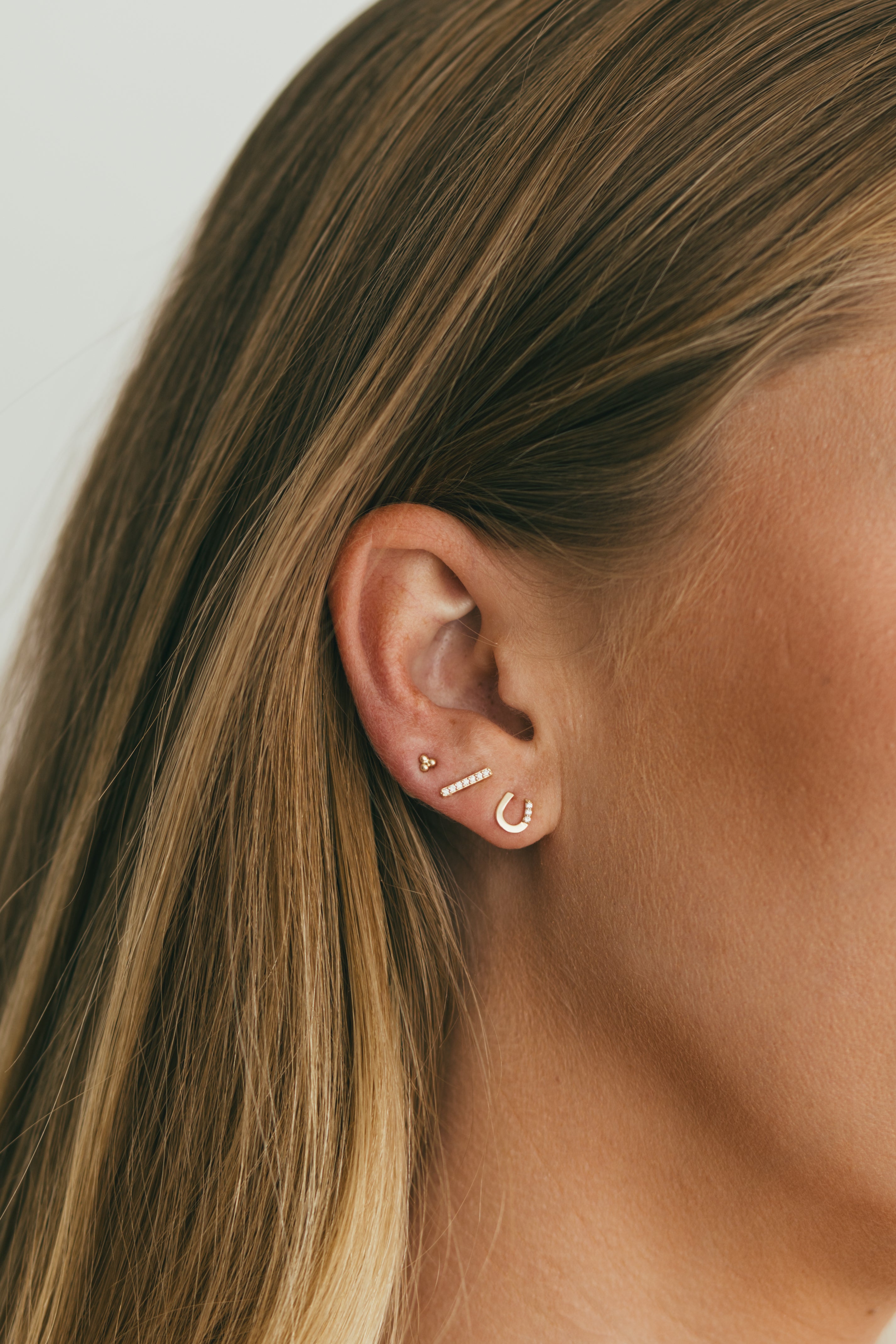 girl wearing an earring stack of horseshoe stud, diamond bar stud, and gold trio stud