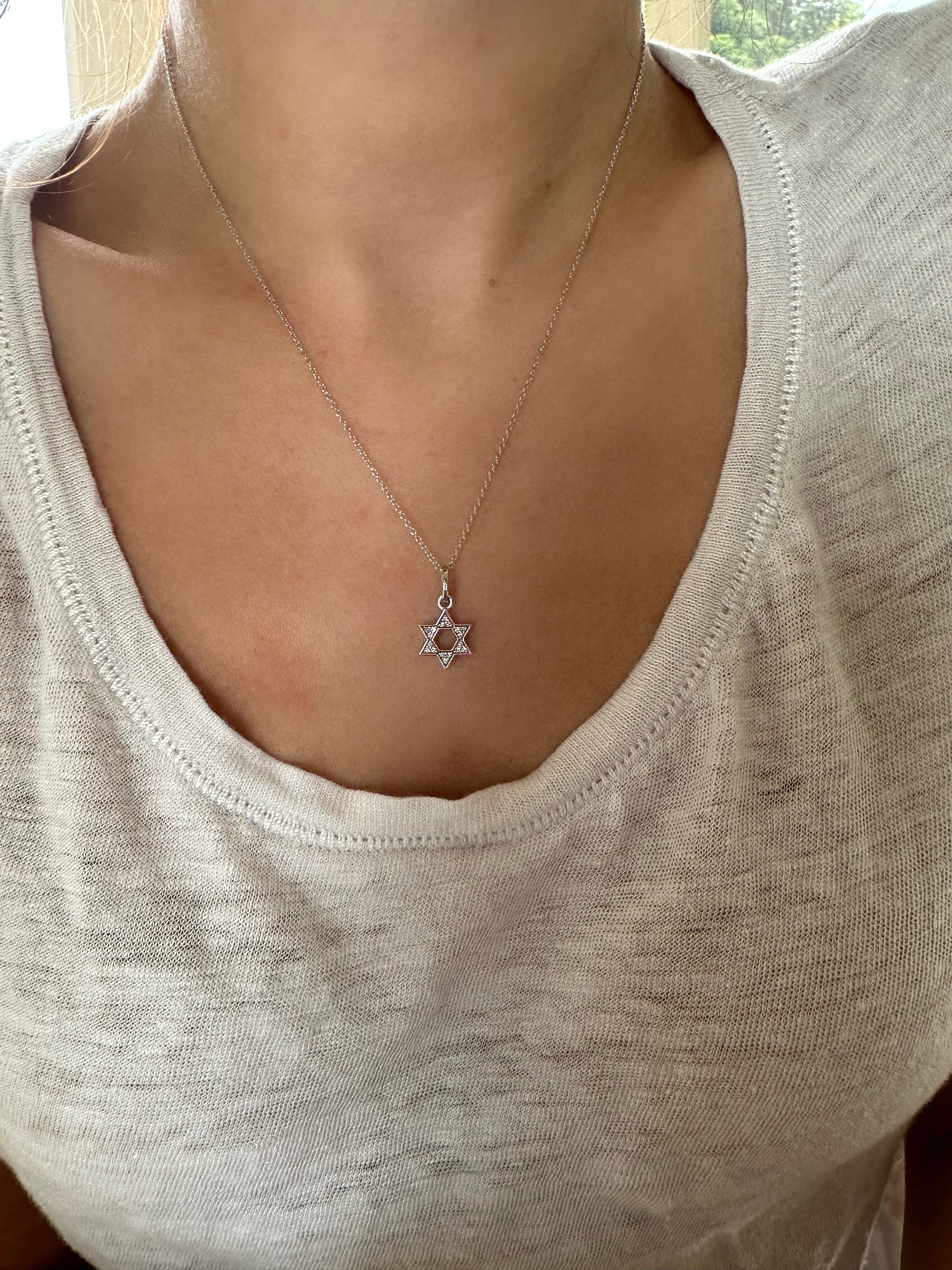 close up of person wearing a white gold small diamond star of david pendant on a chain