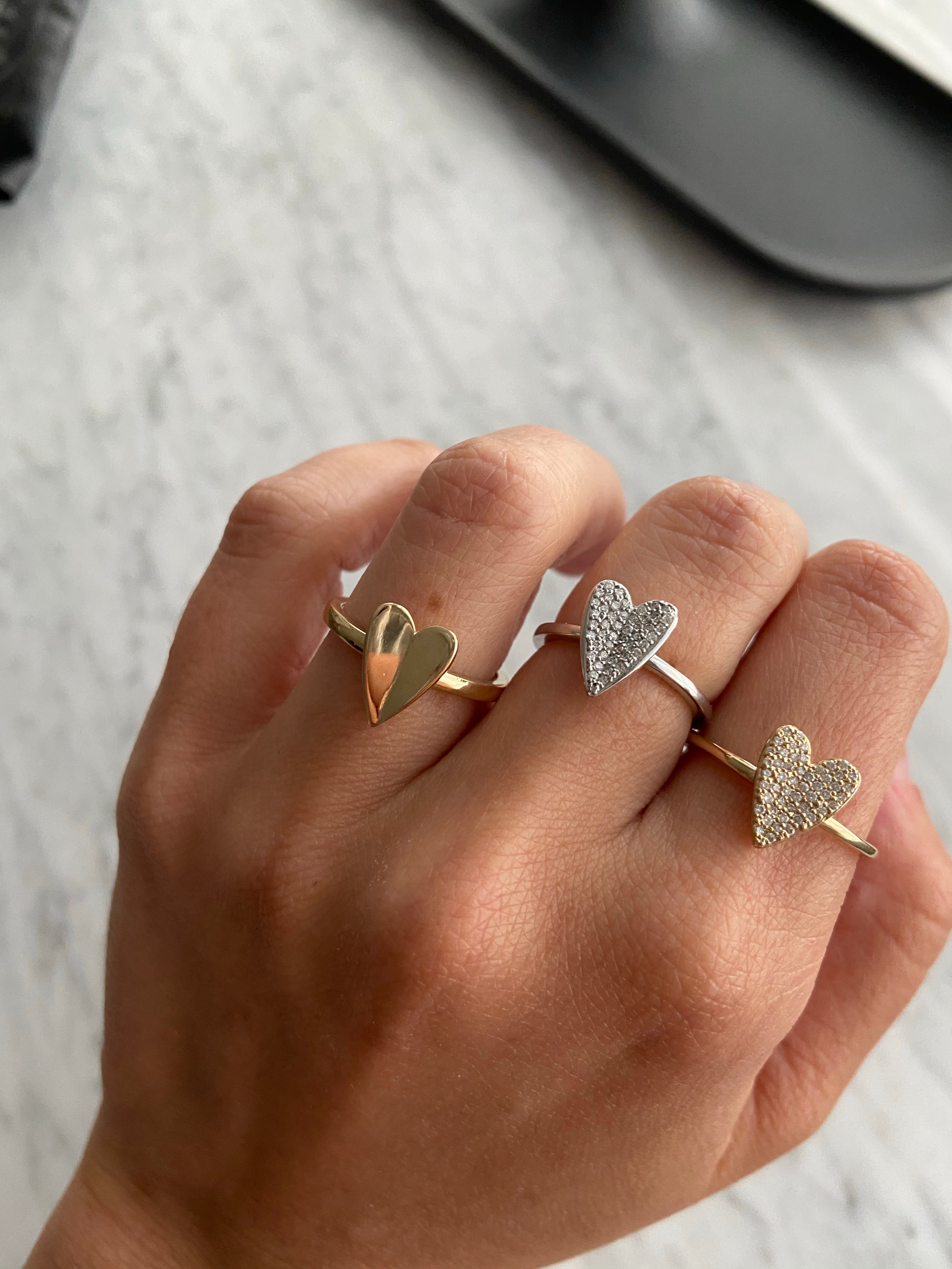 Gold heart rings styled on a person's hand with a grey marble background