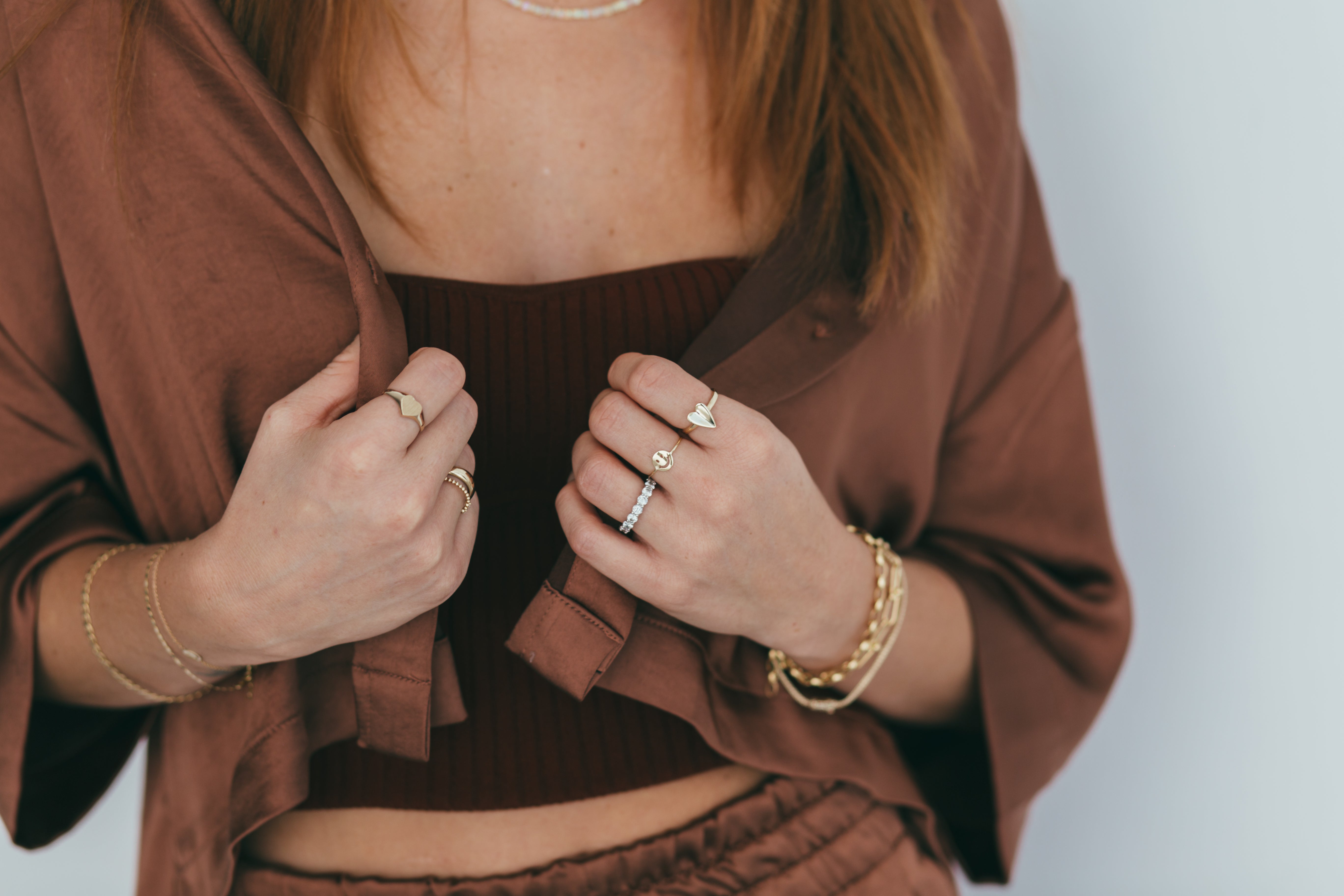 Gold rings and bracelets styled on a person wearing a brown blouse and matching pants