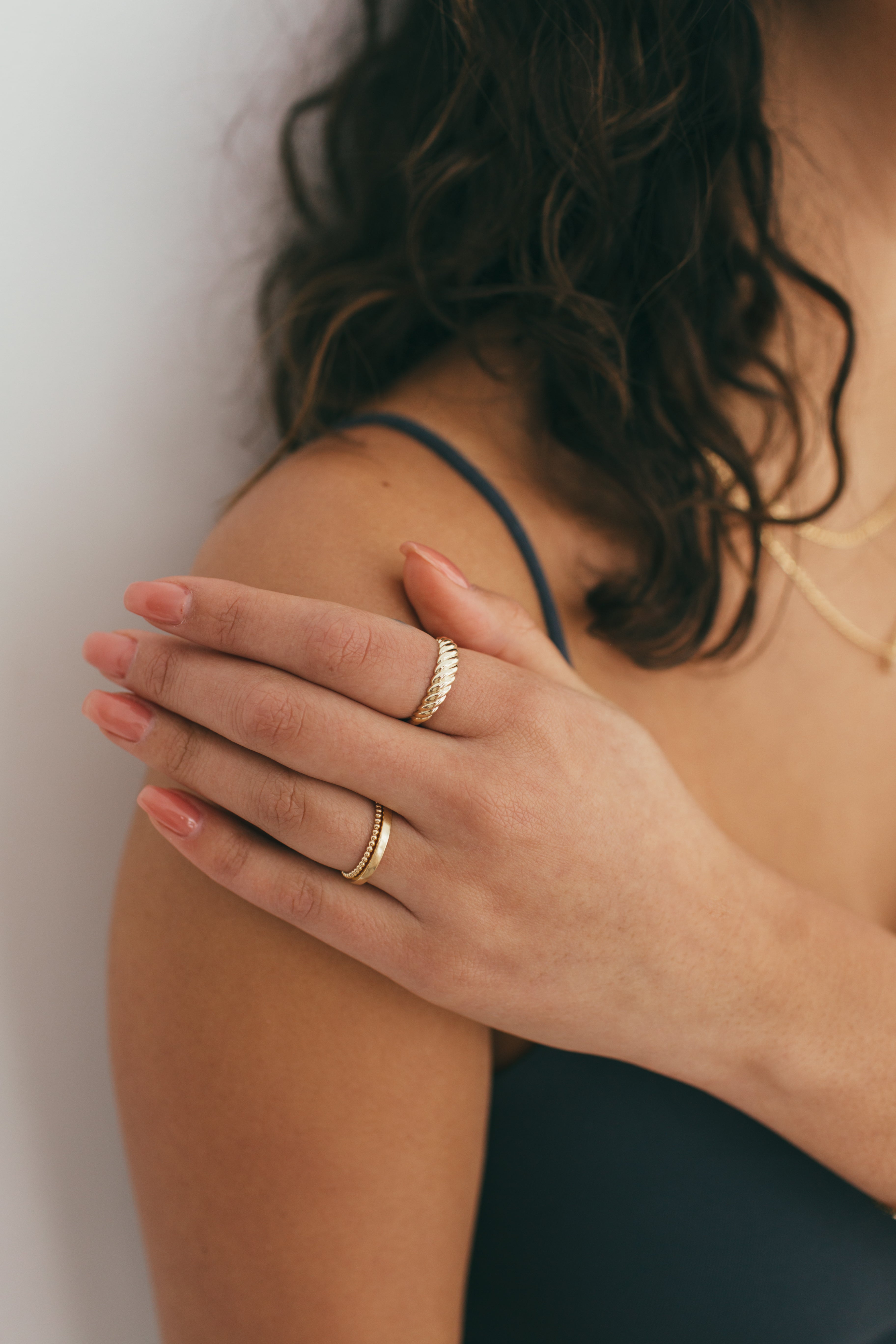 A woman's hand resting on her shoulder styled with yellow gold rings.