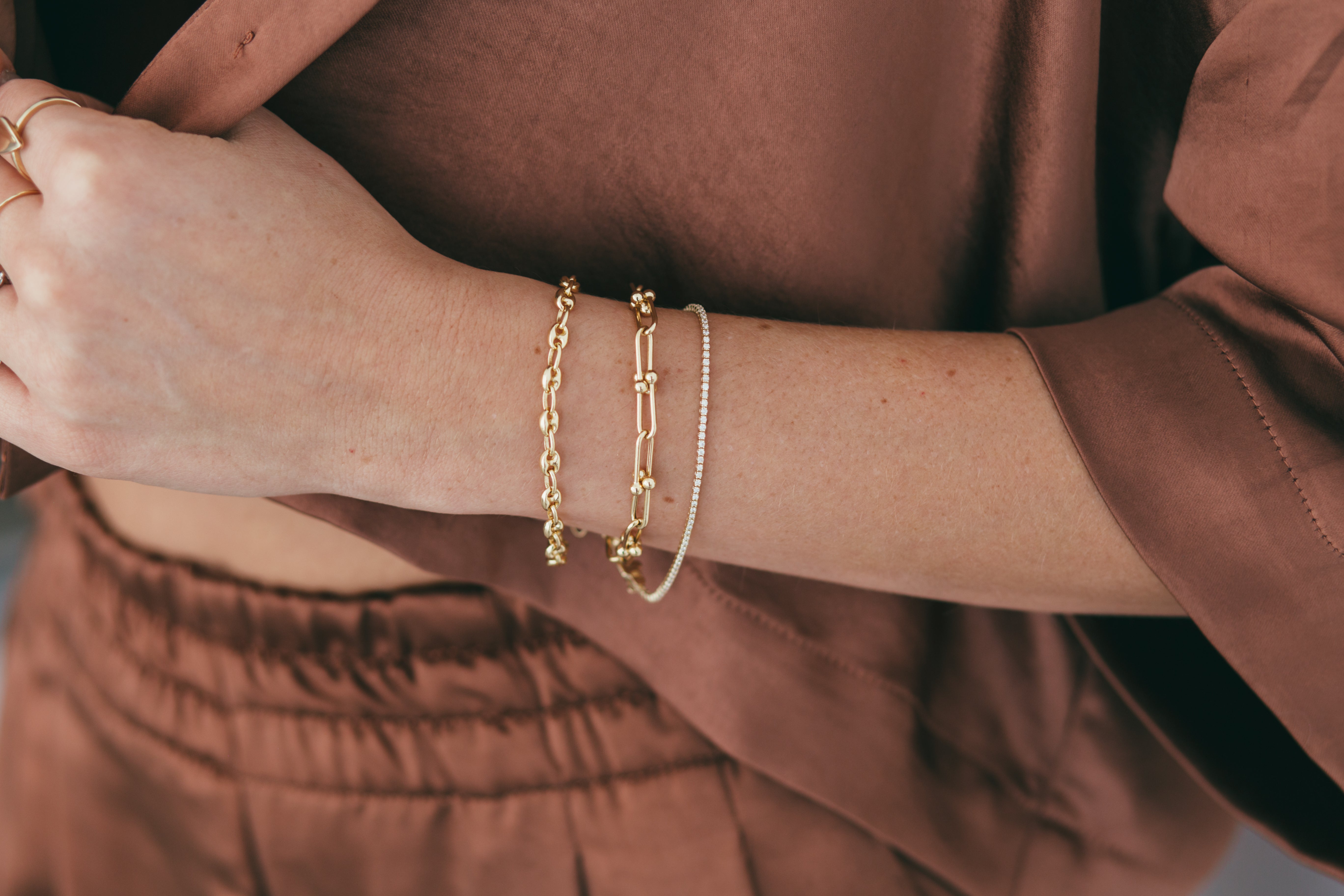 Puffy anchor bracelet worn on model, stacked with another gold bracelet and tennis bracelet. 