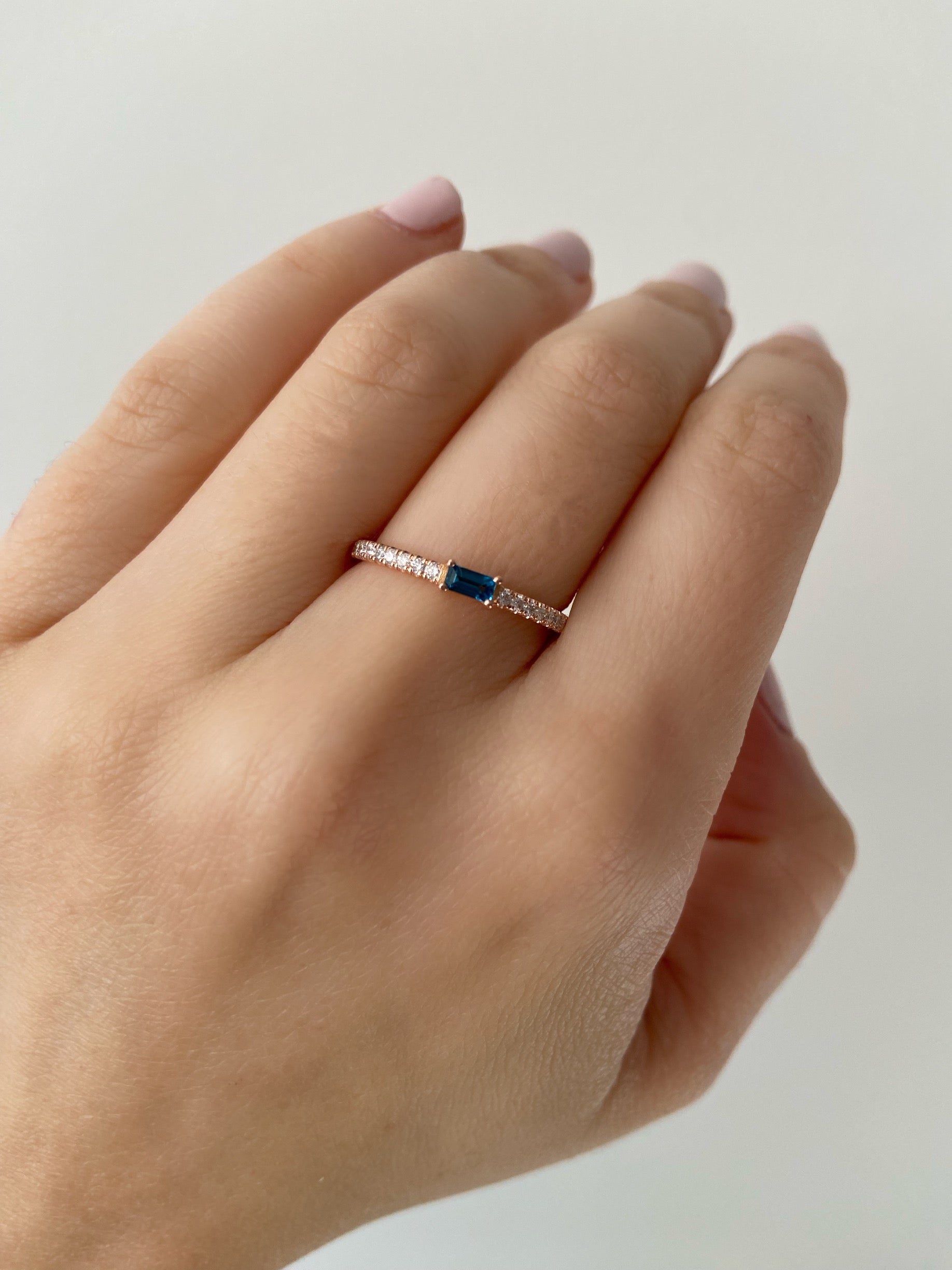 Hand wearing a baguette birthstone and diamond ring on a neutral background.