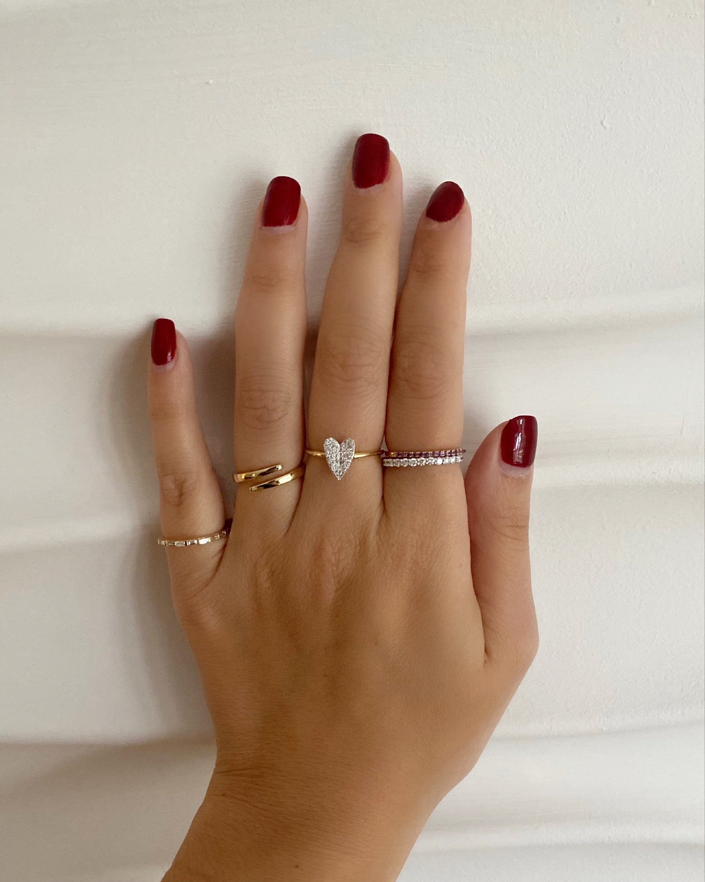 A woman's hand wearing multiple gold and diamond rings, on a textured ripple white background.