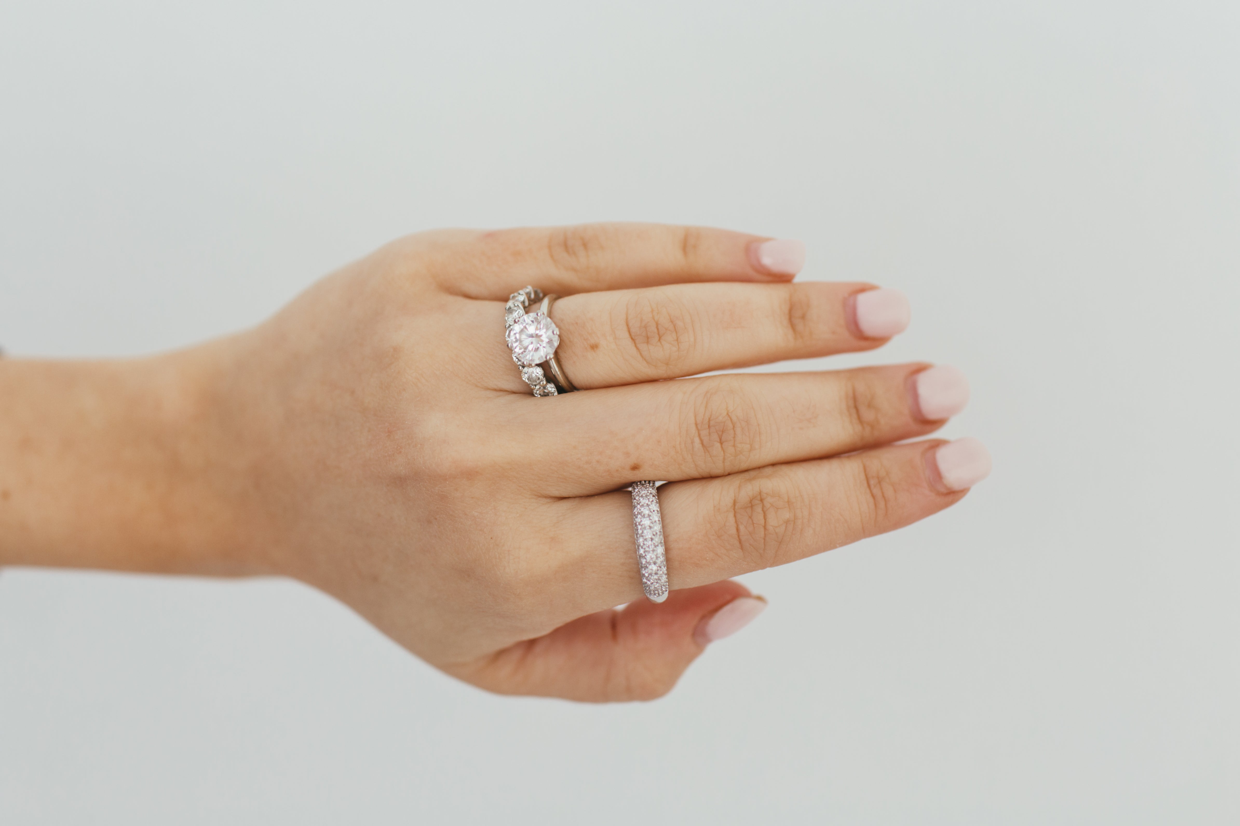 Close up of a hand wearing a gold diamond dome ring and other diamond rings on a white background.