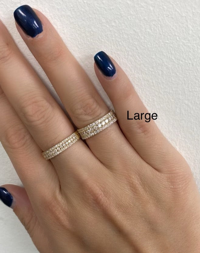 A close up of a woman's hand wearing a yellow gold large triple row pavé along with a smaller yellow gold triple row pavé ring.