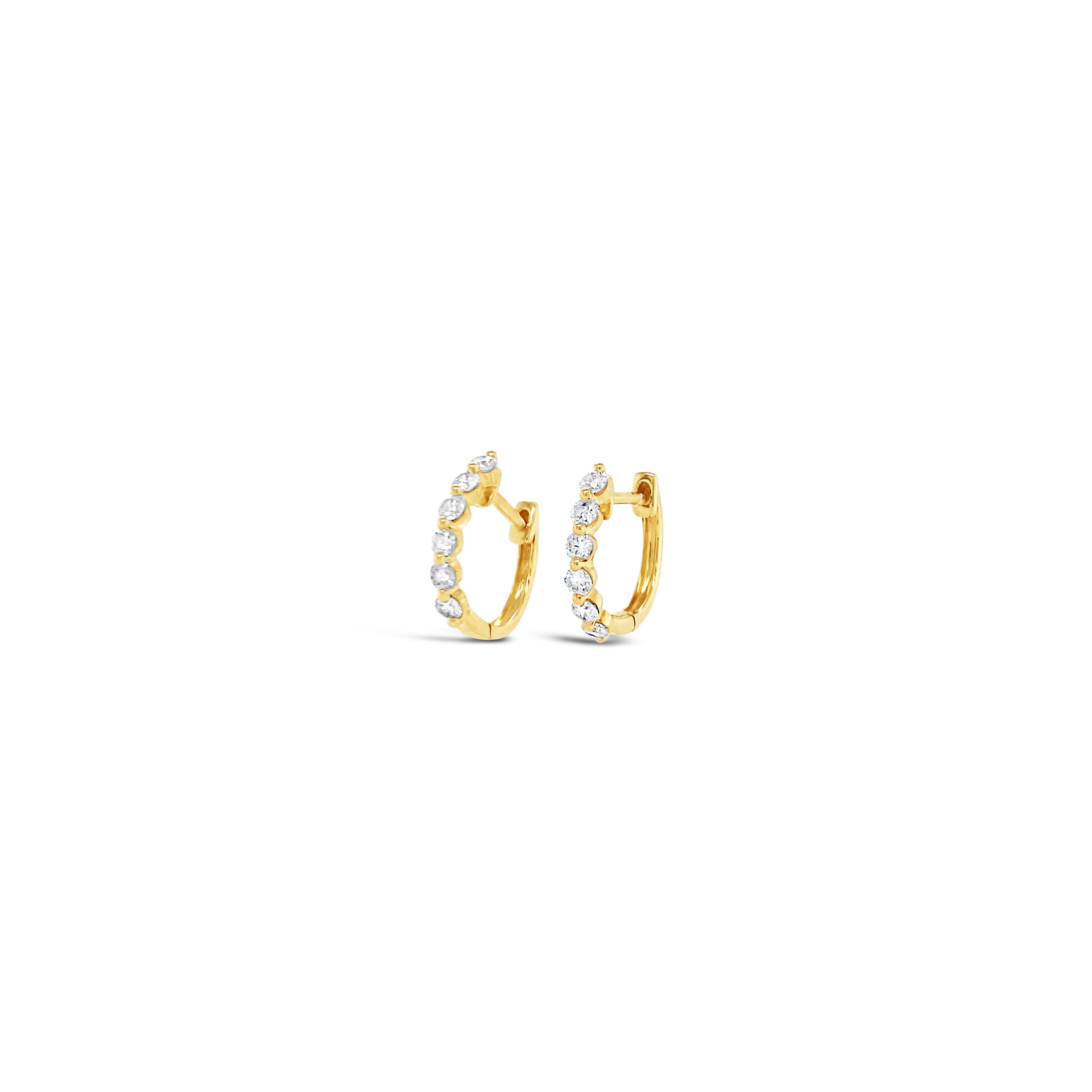 A pair of 14K gold single prong diamond huggie earrings on a white background.