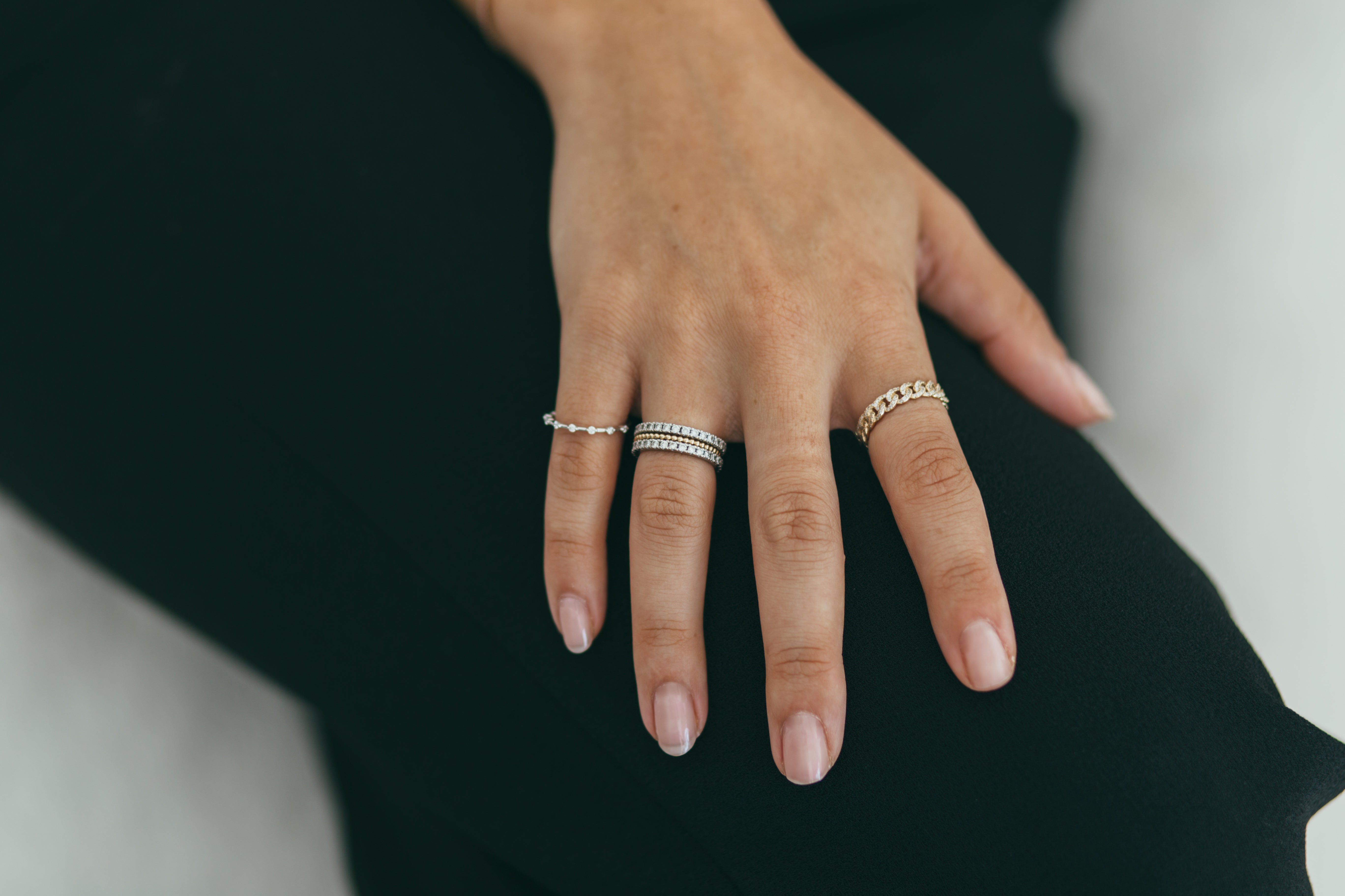 A close up of a hand wearing a mix of gold and diamond rings with a blurred background.