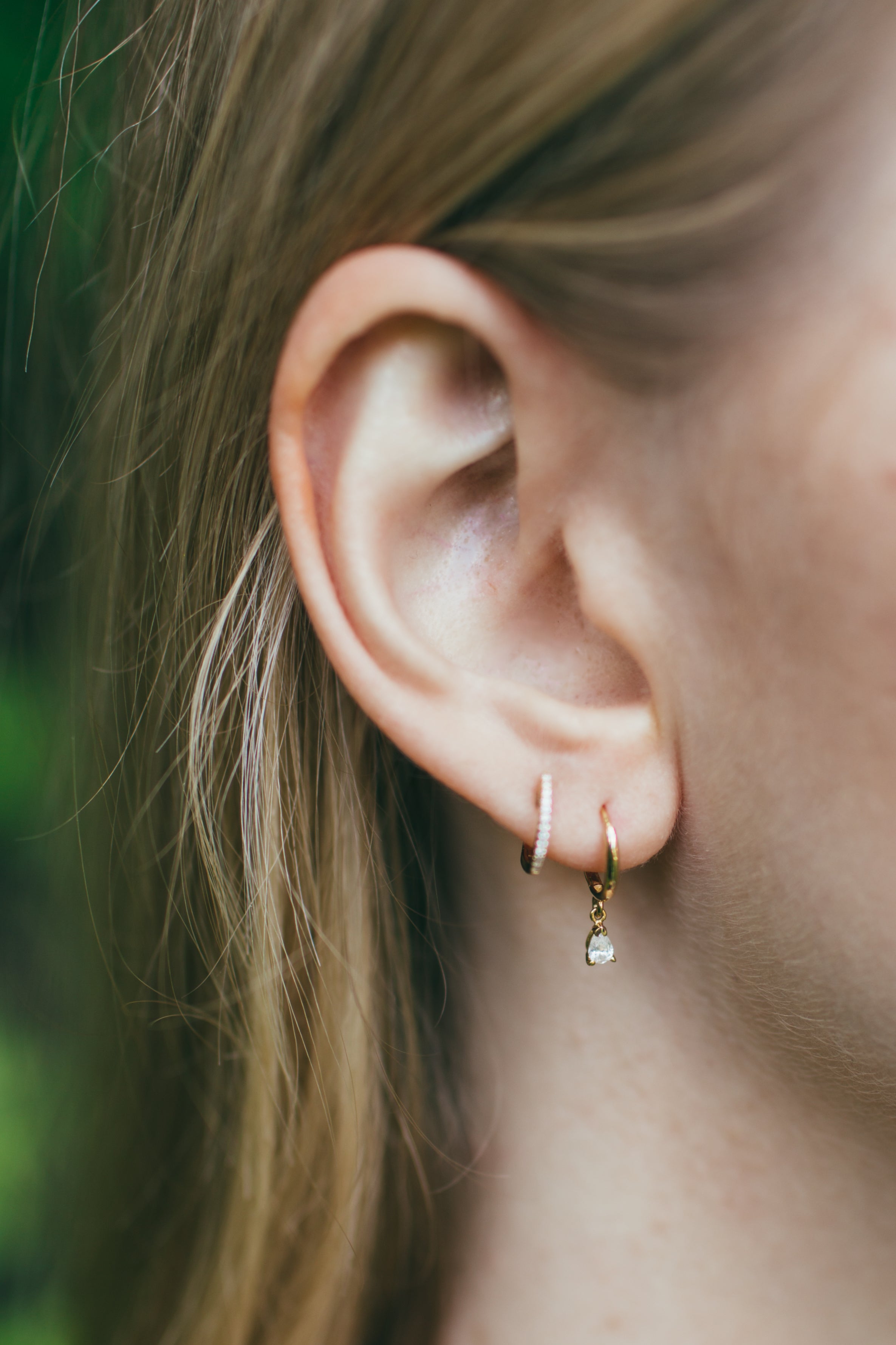 close up of girls ear wearing dangling pear diamond huggies and pave diamond huggies 