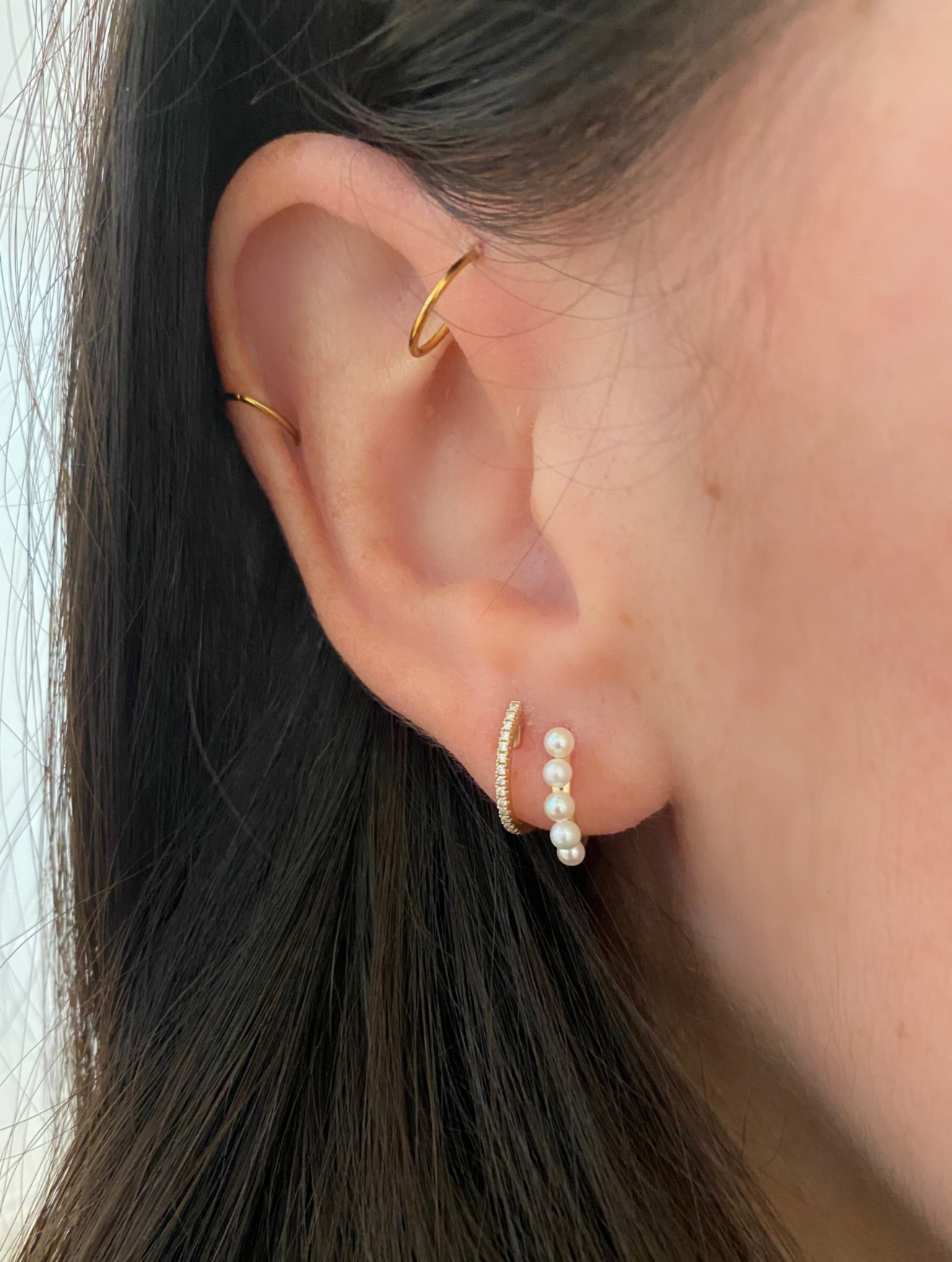 close up of earring stack of diamond huggie and pearl huggie