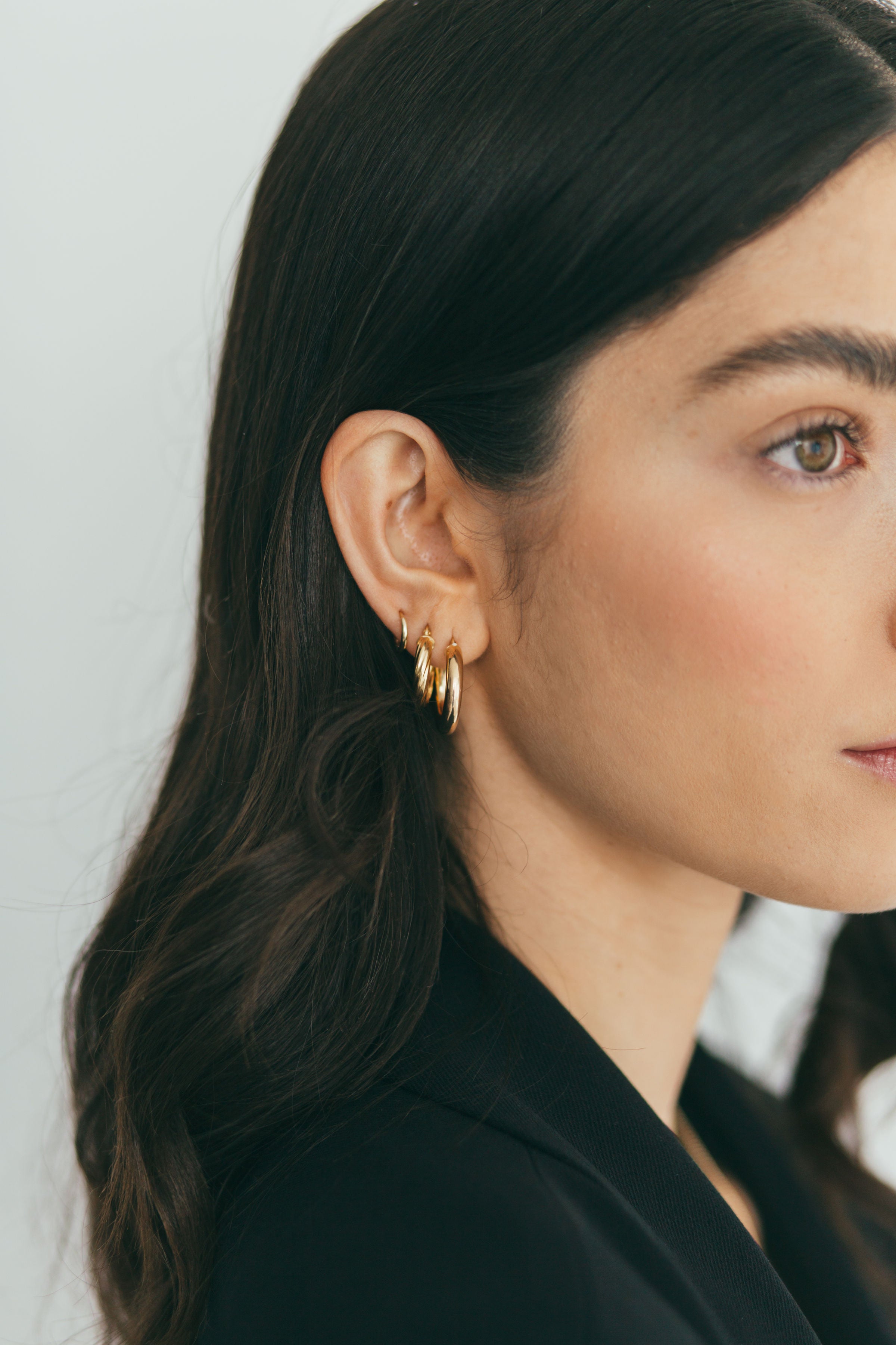 a girl wearing gold hoops, twisted hoops, and mini gold huggies 