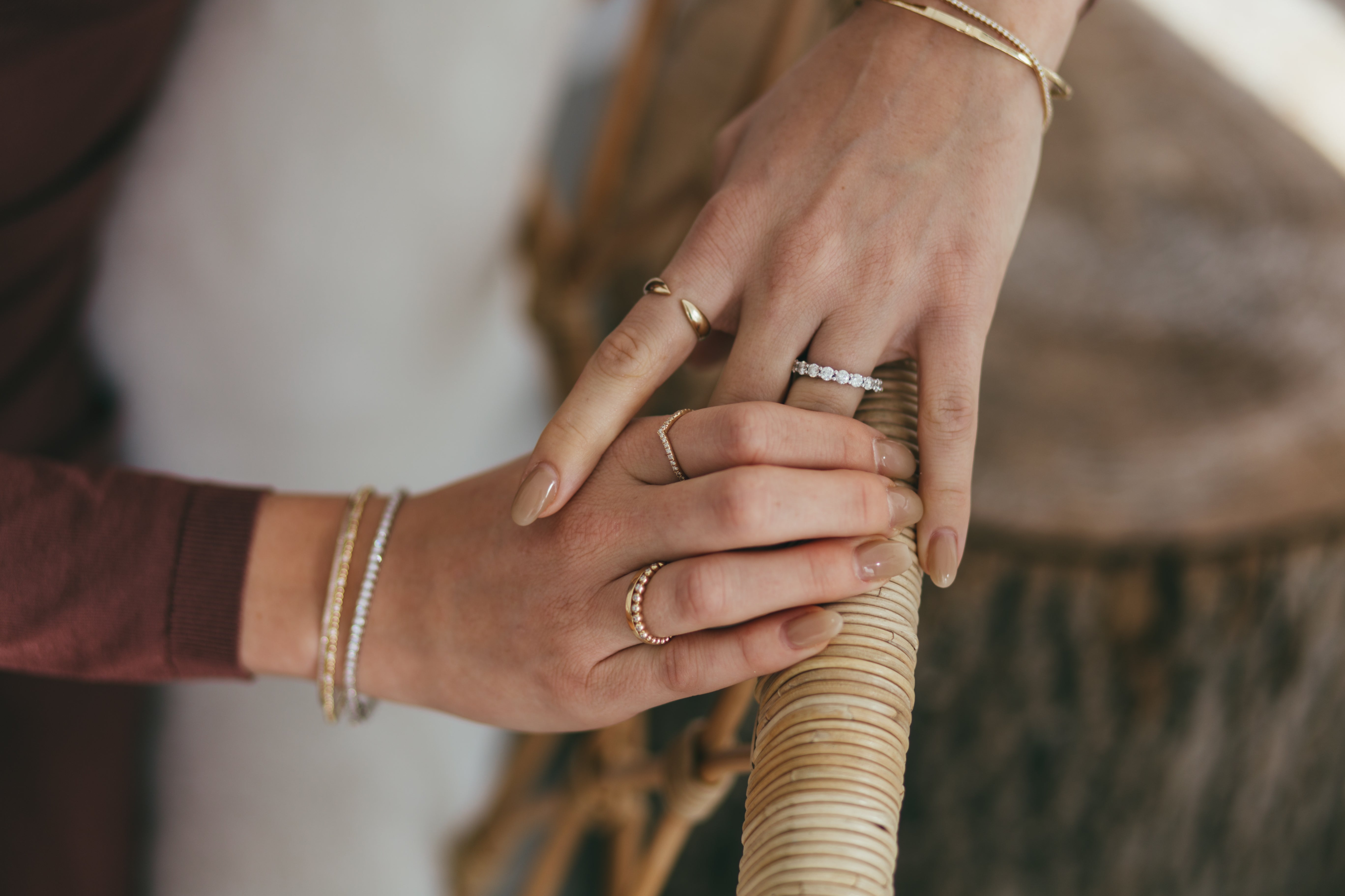 A person's hands accessorized with a mix of gold and diamond rings and bracelets on a blurred neutral background.