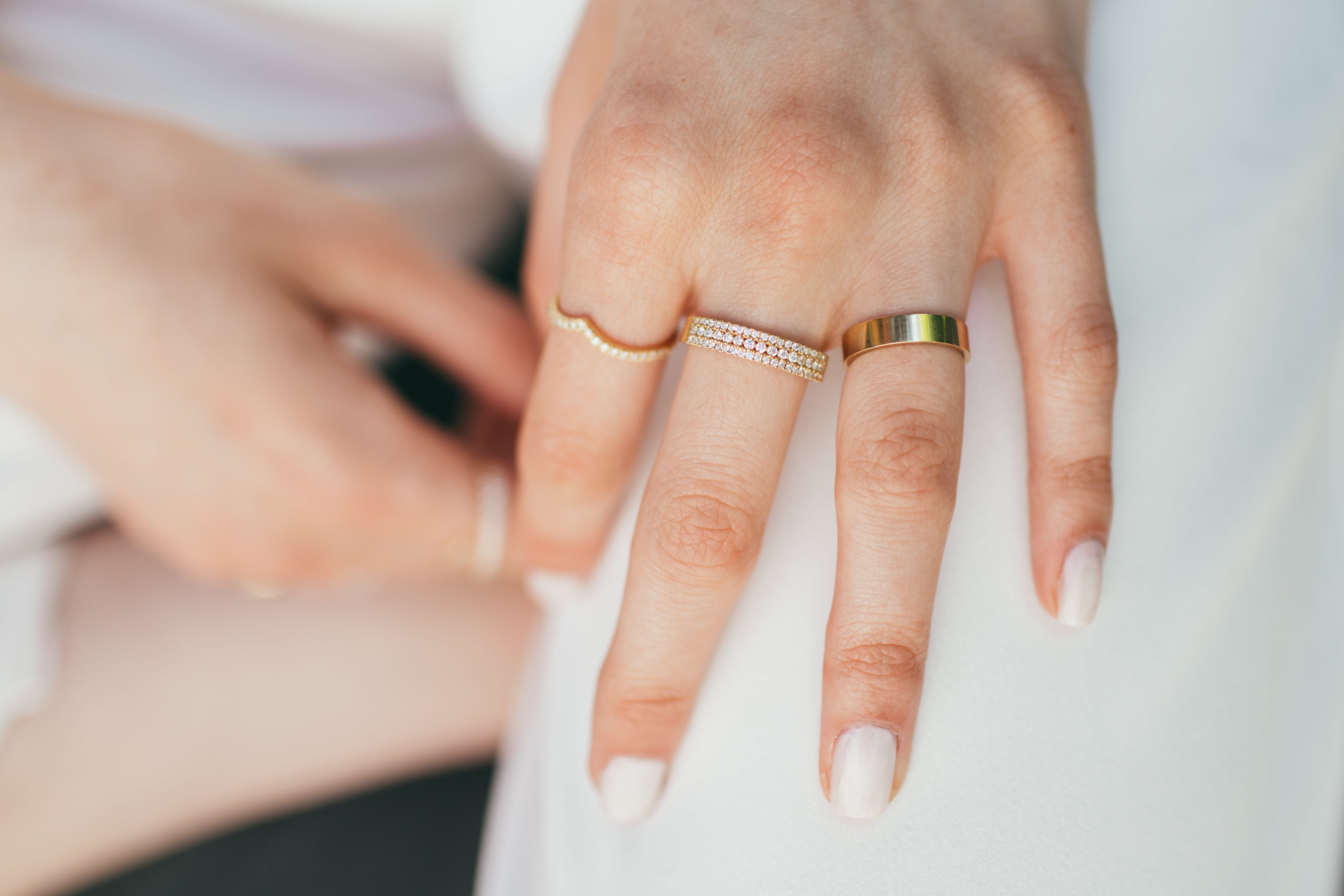 A close up of a hand wearing a diamond v ring and other diamond and gold rings on a blurred background.