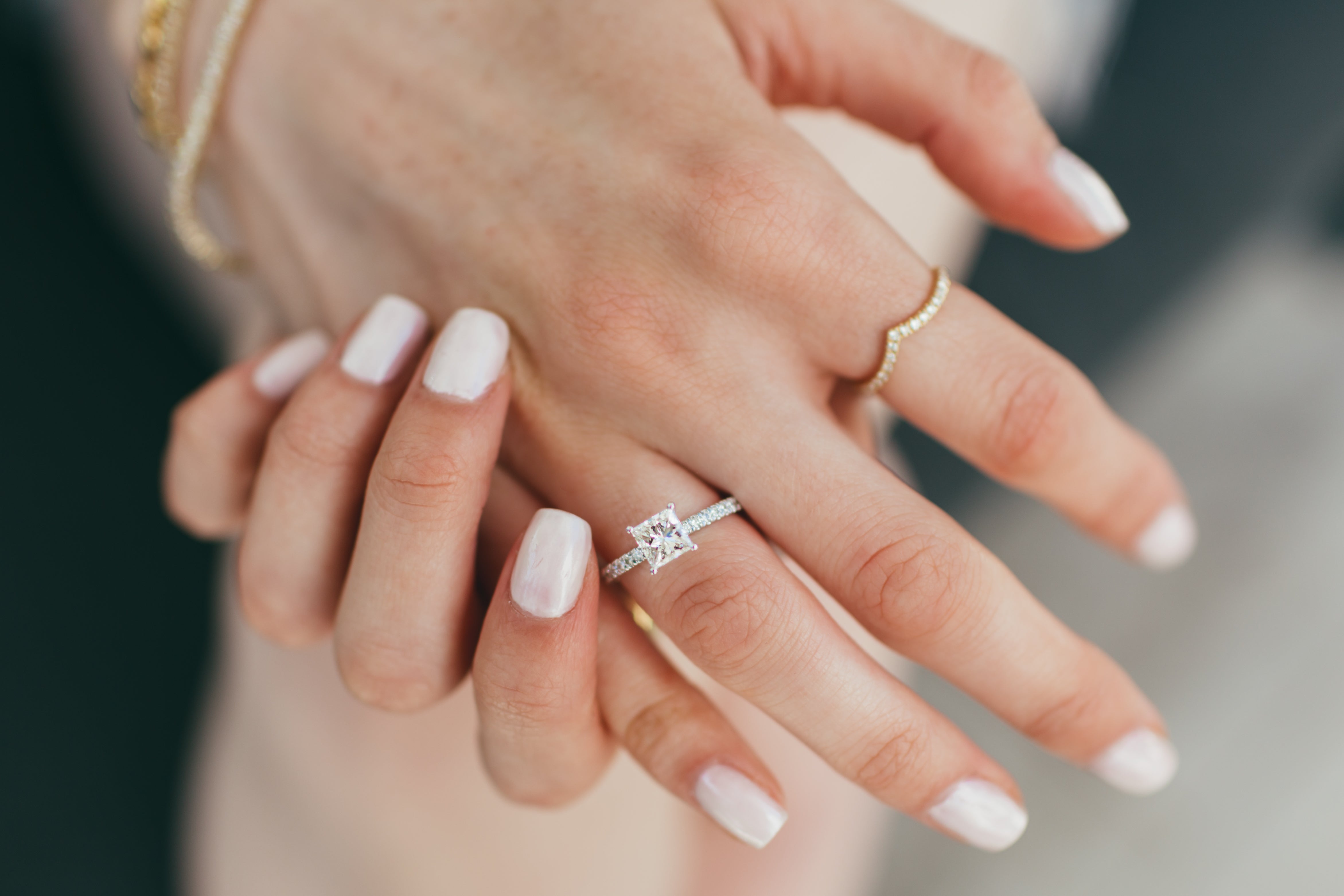 A close up of a woman's hands styled with a diamond v ring and other diamond ring on a blurred background.