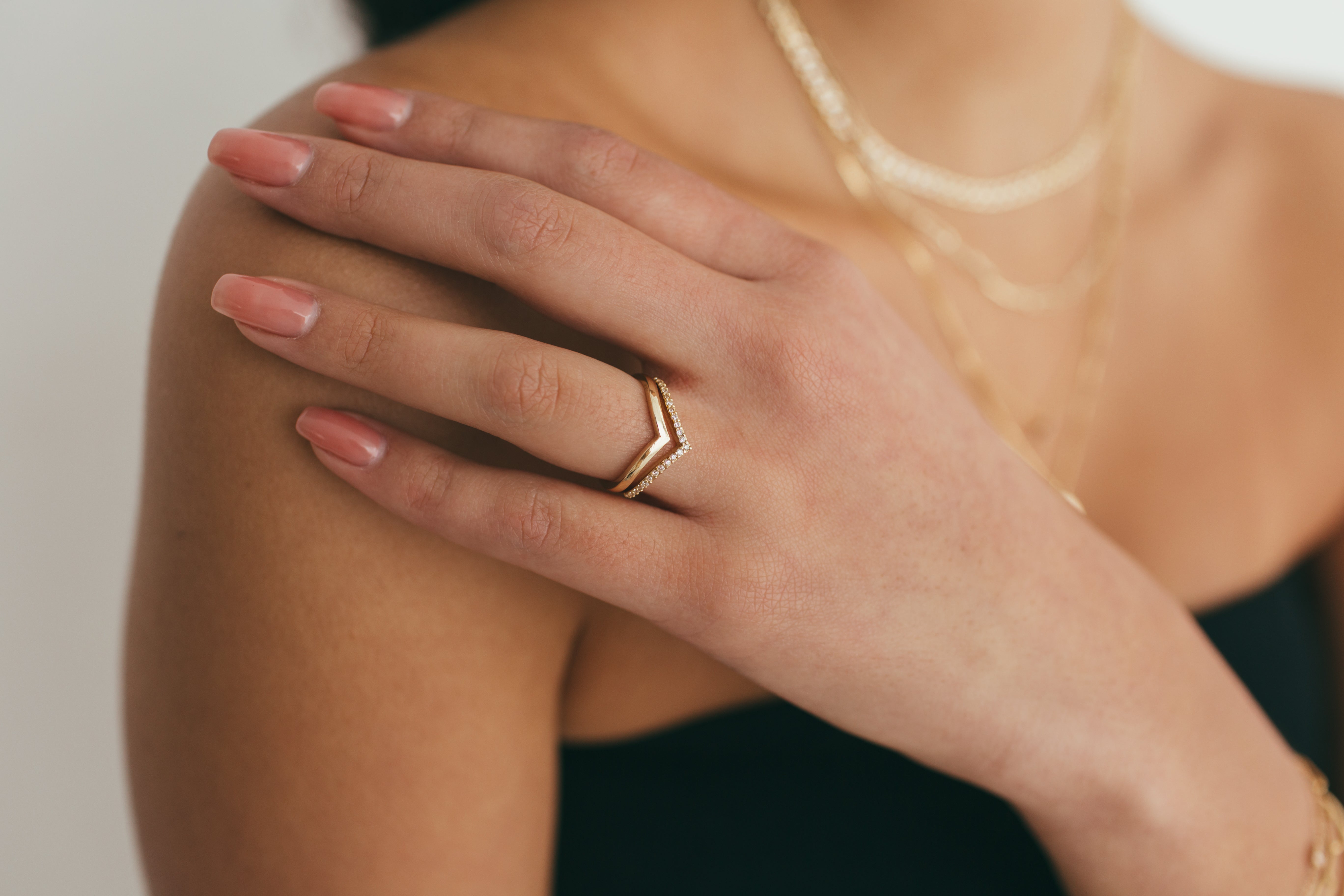 A woman's hand resting on her shoulder, styled with a simple yellow gold v ring and diamond v ring.