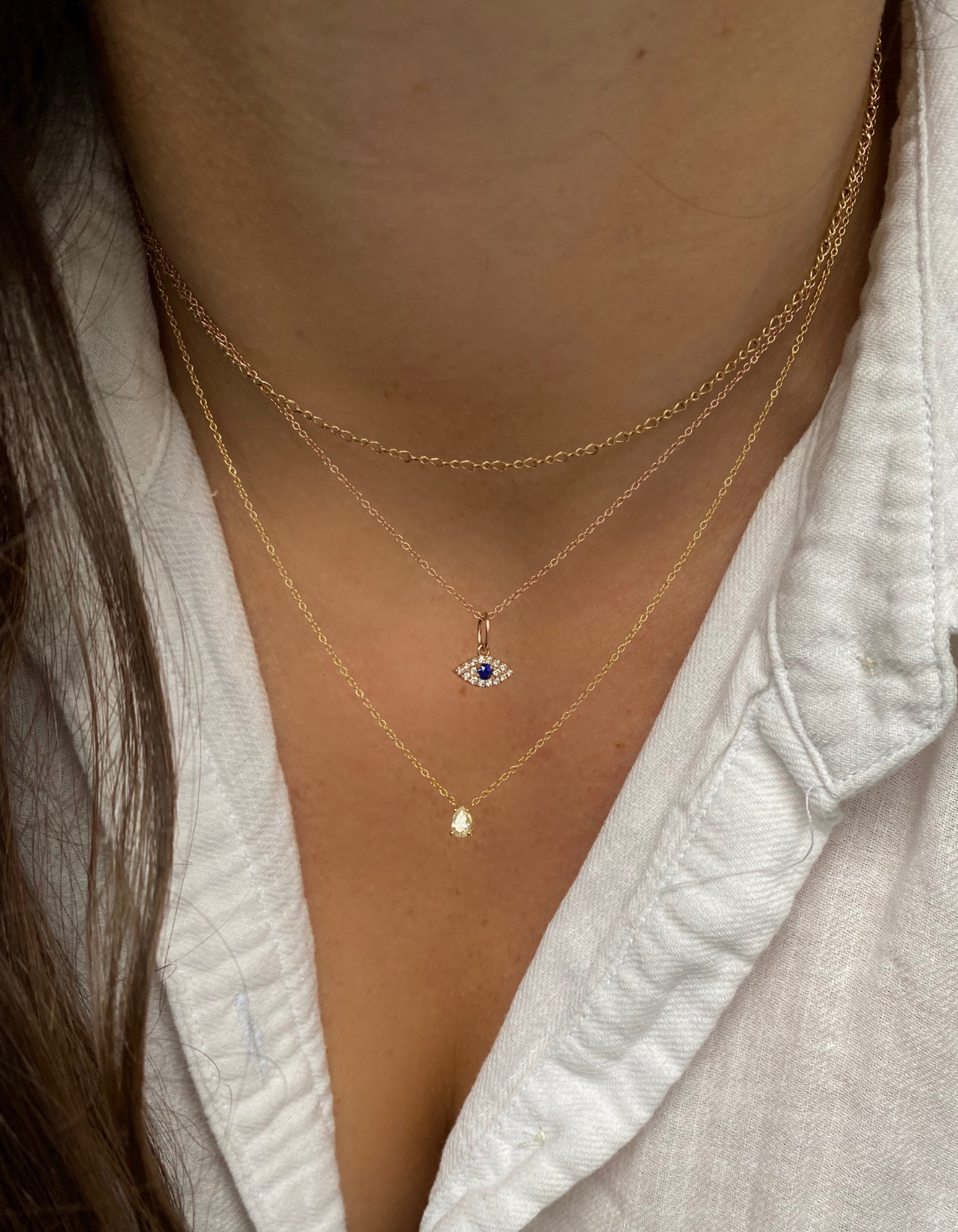 close up of a person layering three chains including a diamond and sapphire evil eye pendant 