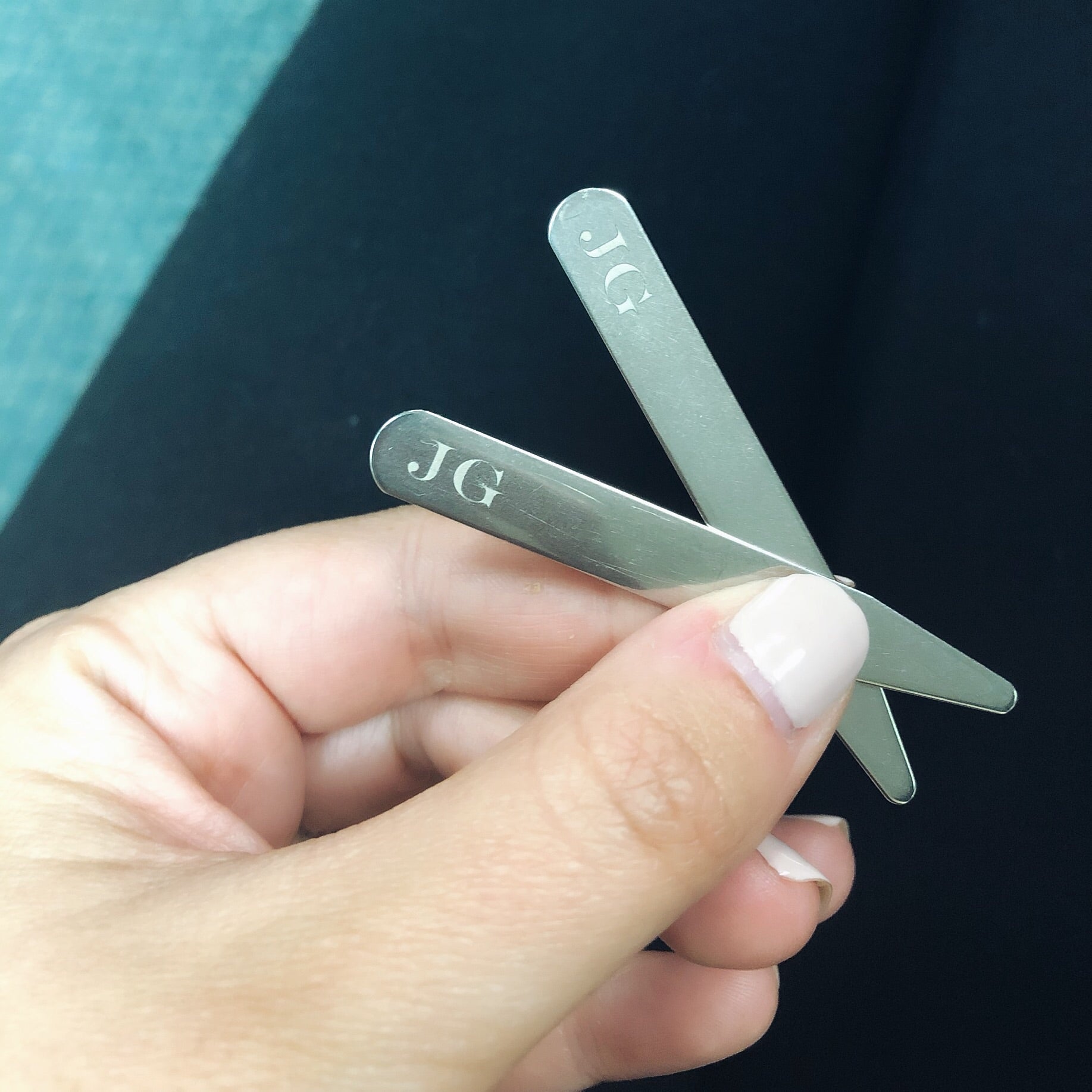 A close-up of engravable collar stays with the initials "JG".