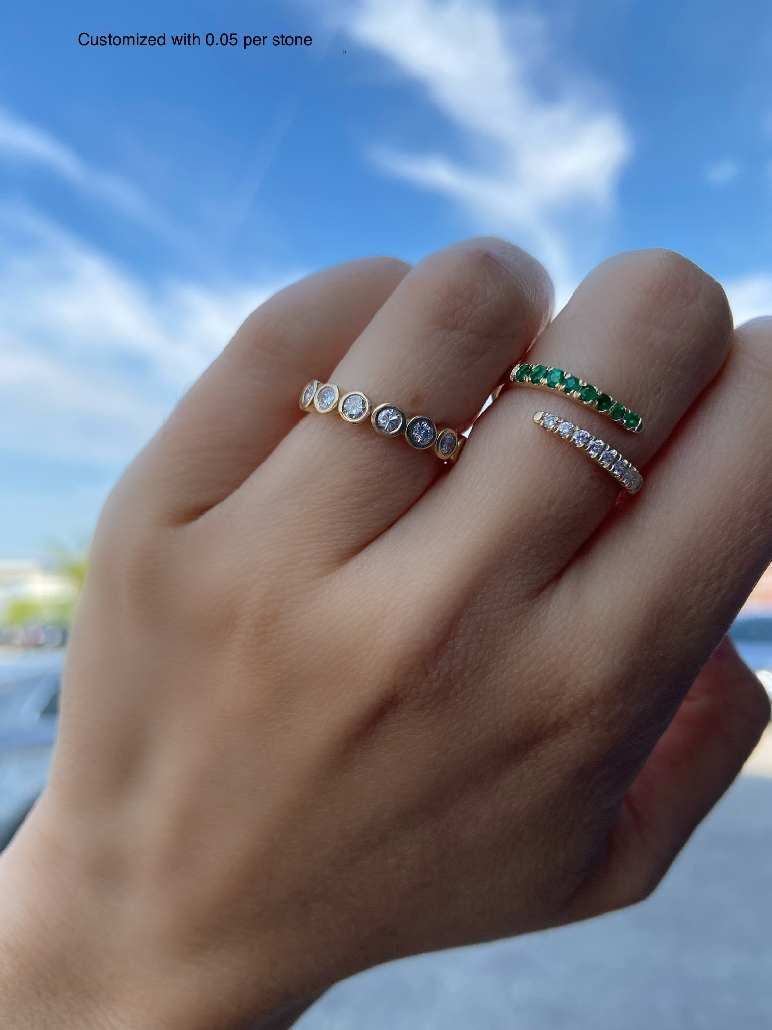 A close up of a lab grown diamond bezel ring on a person's hand with clouds in the background.