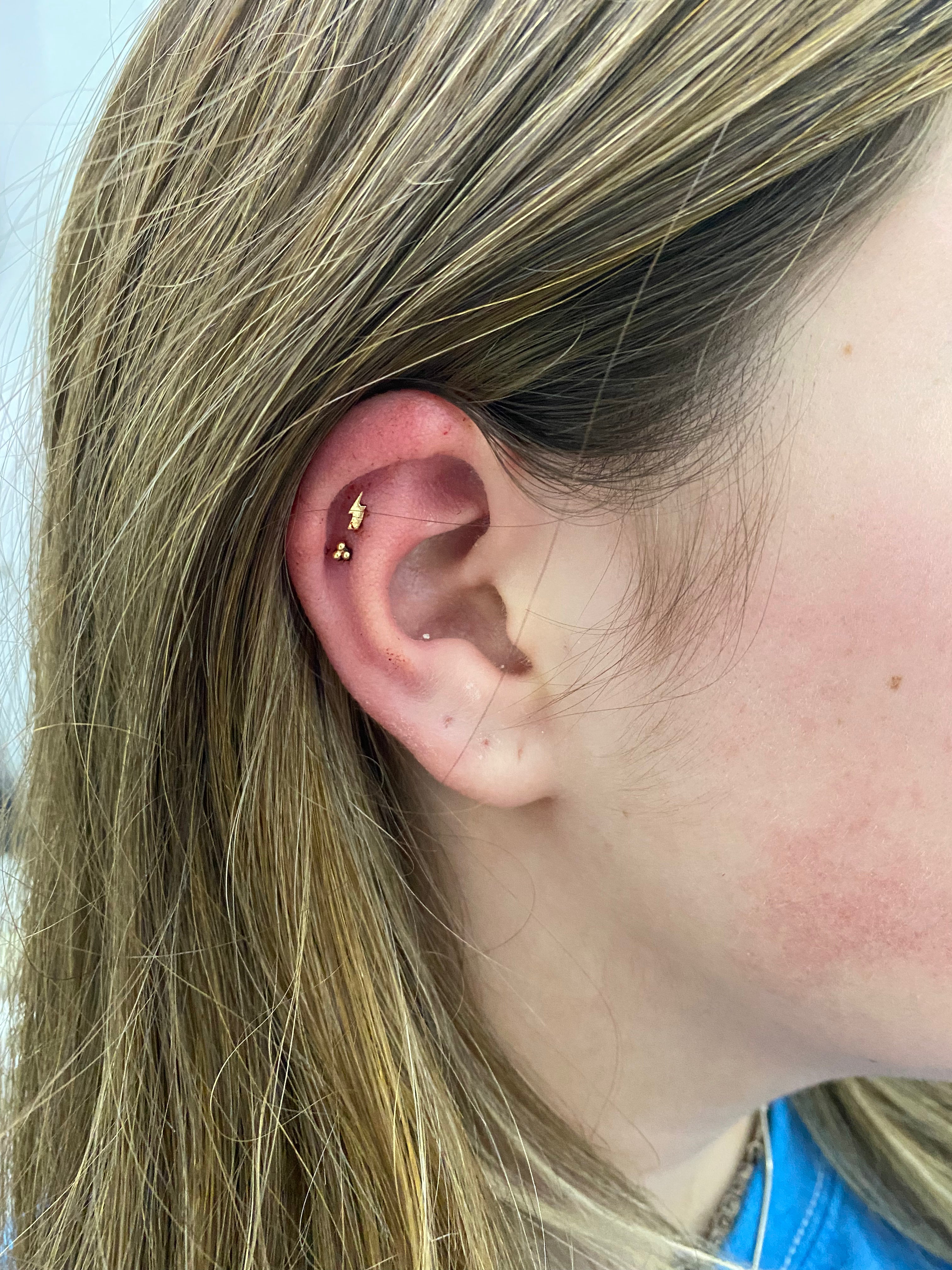 close up of ear wearing gold trio studs and lightning bold stud